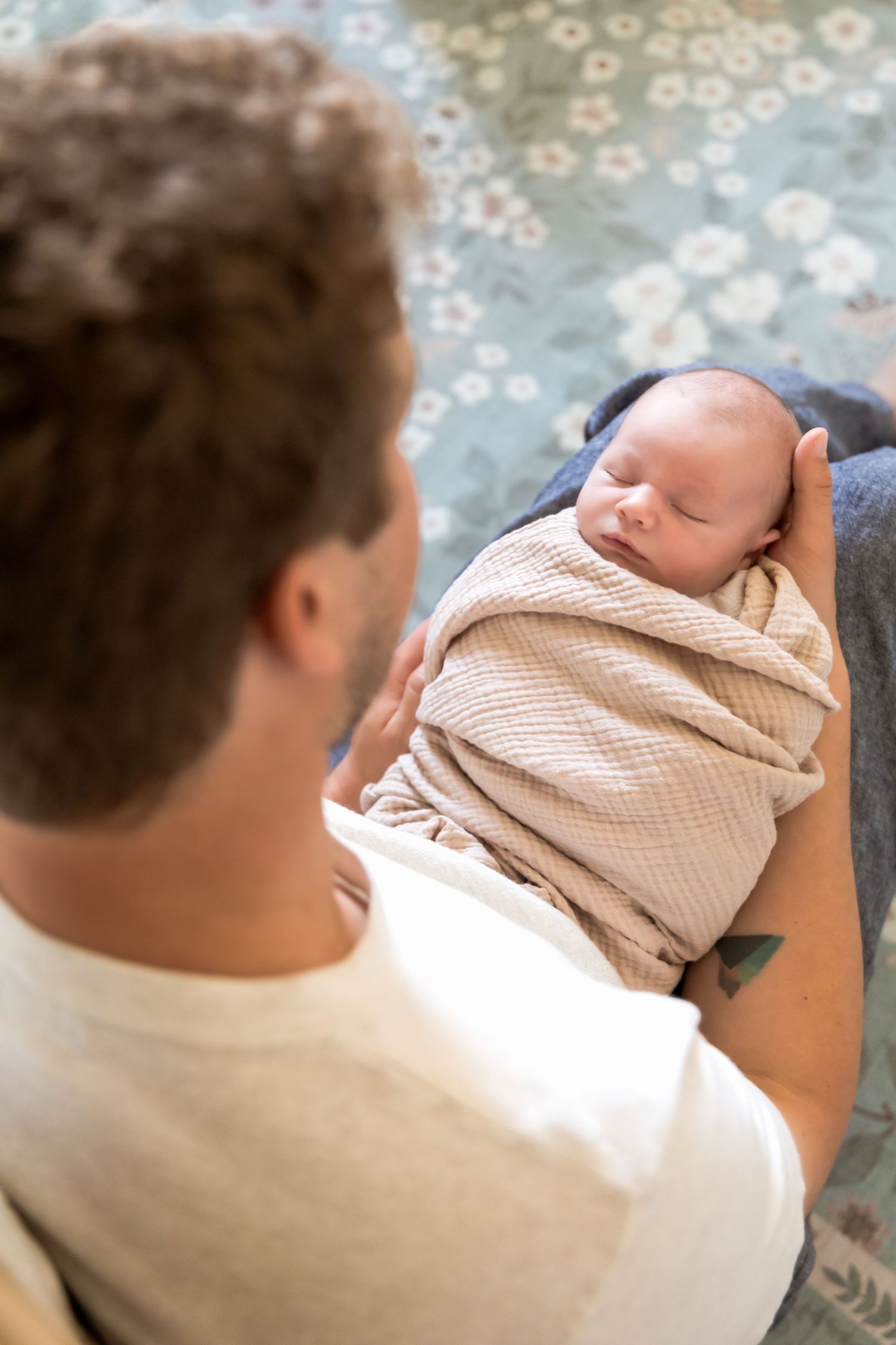 Father gazes lovingly at sleeping swaddled newborn baby cradled in his arms.