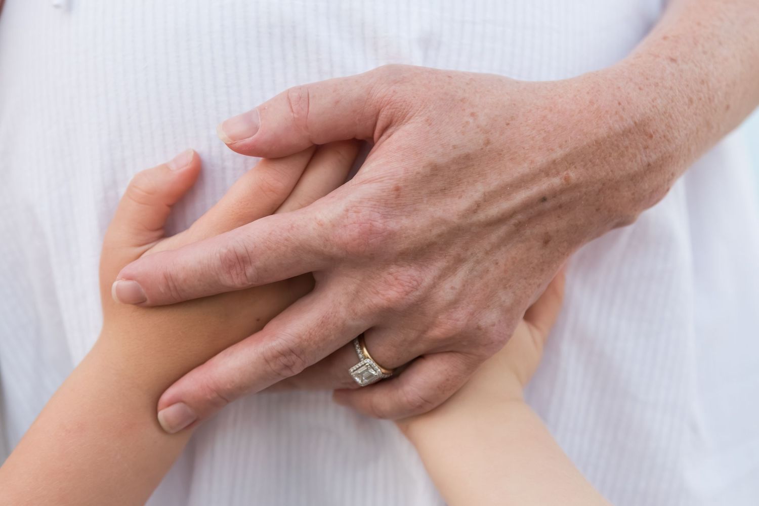 Close-up of an older couple holding hands, woman wearing a diamond engagement ring, symbolizing love and commitment.