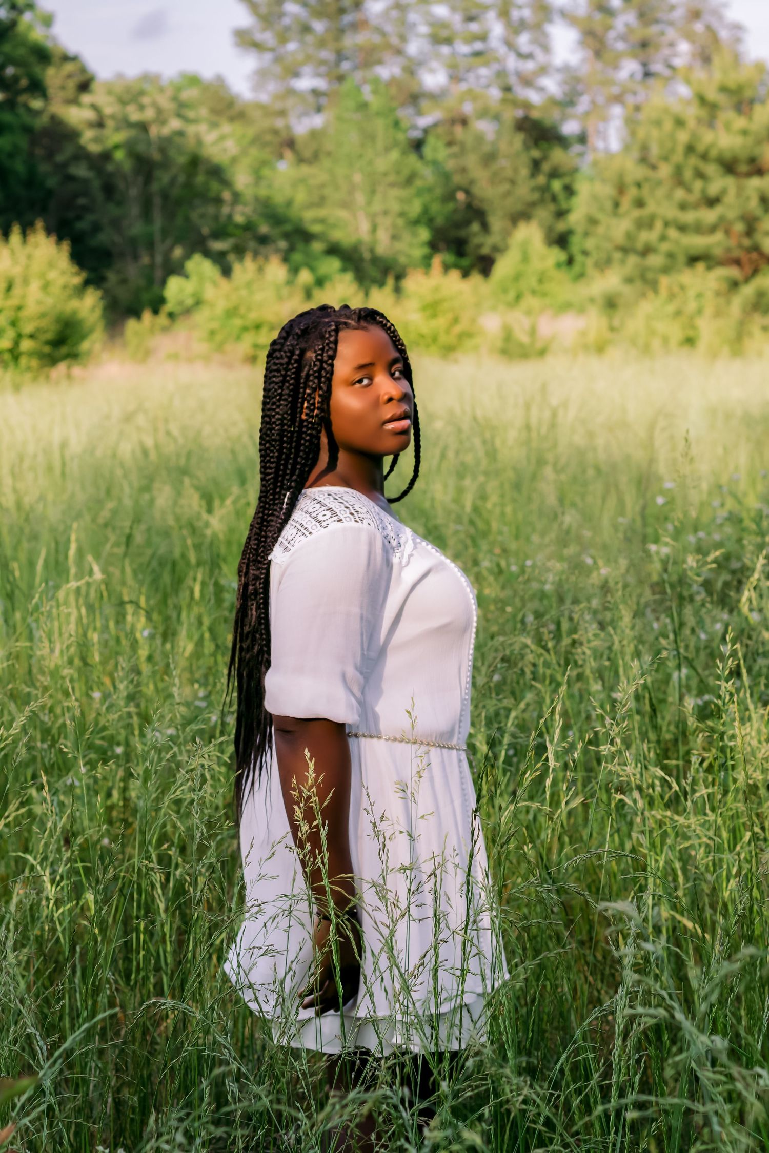 Woman in white dress standing in tall summer grass during golden hour.