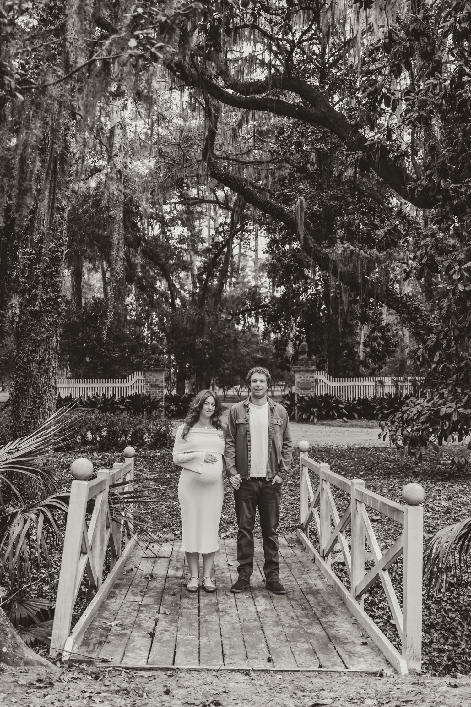 A group stands on a wooden bridge walkway surrounded by lush trees and greenery in an outdoor setting.