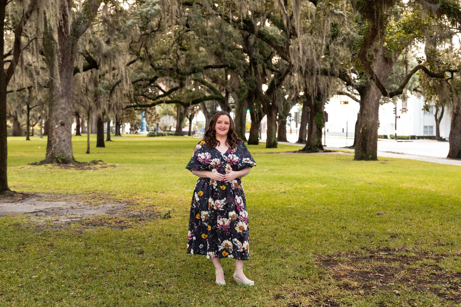 A person walks their dog through a scenic park with moss-draped oak trees on a sunny afternoon.