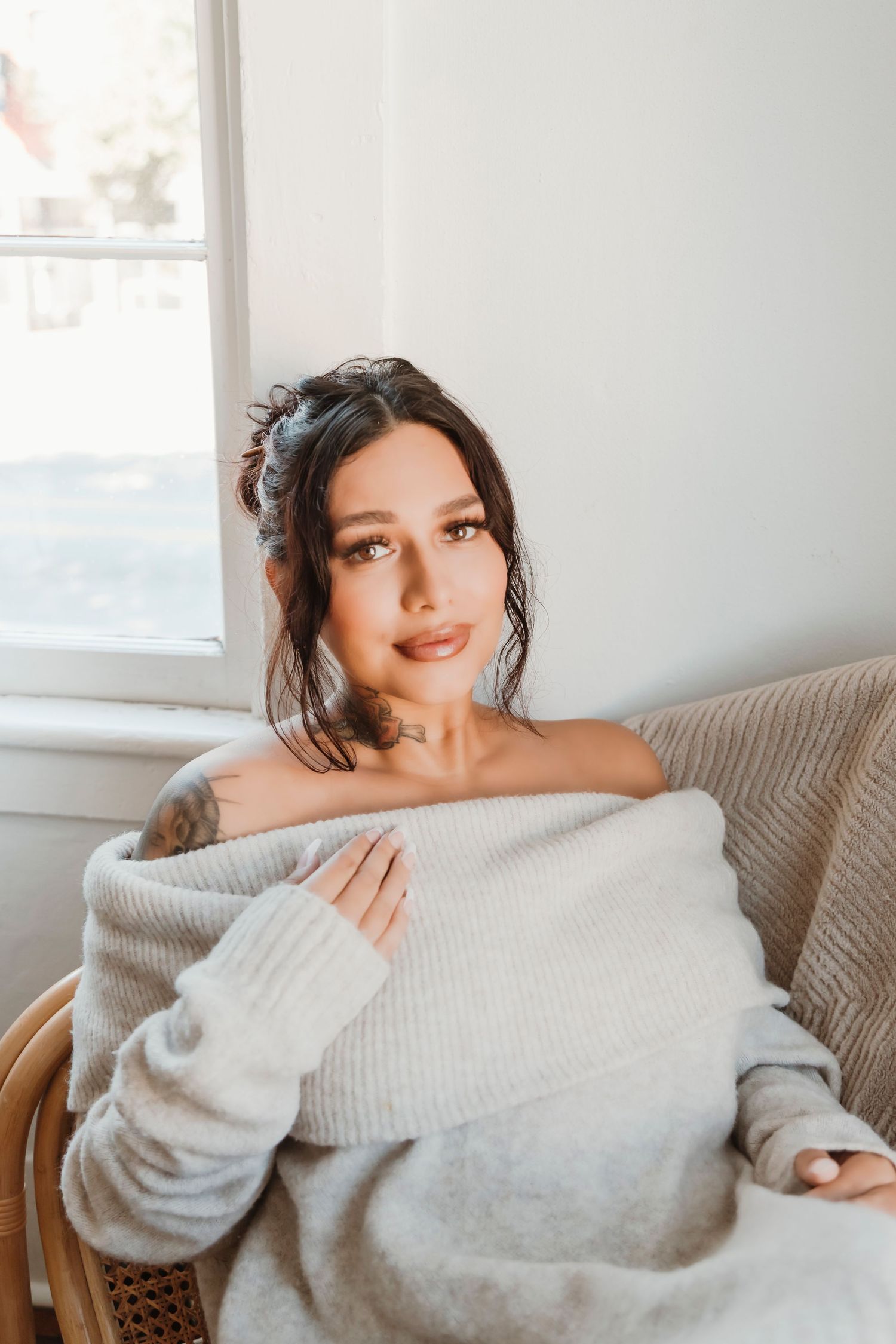 Soft portrait of someone in white sweater sitting by window in natural light.