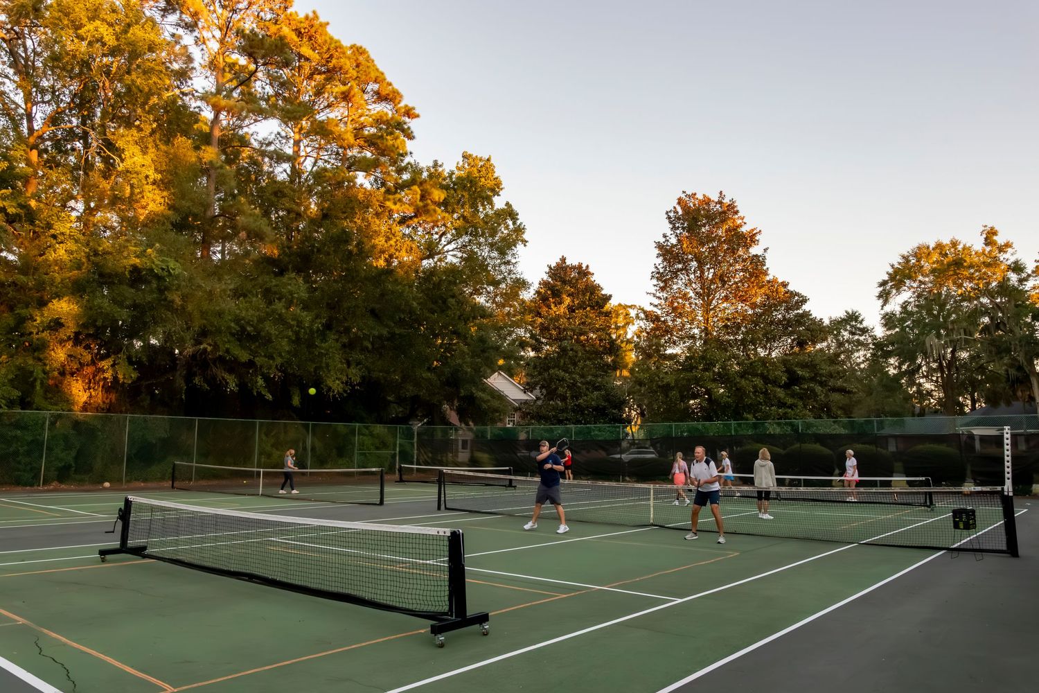 Panoramic view of tennis courts surrounded by fall foliage at sunset.