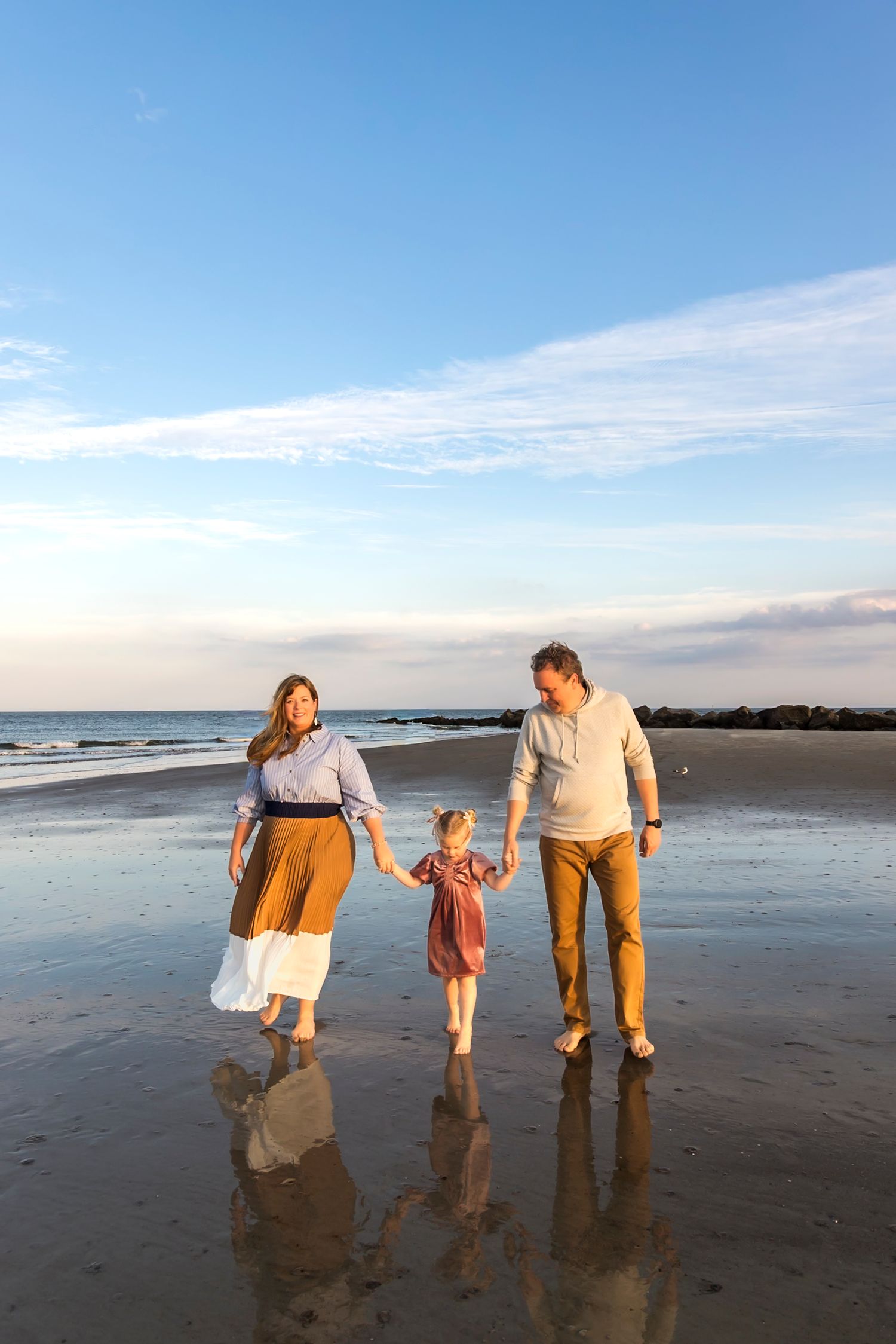 Family walking and playing together on a beach at sunset with reflections in the wet sand.
