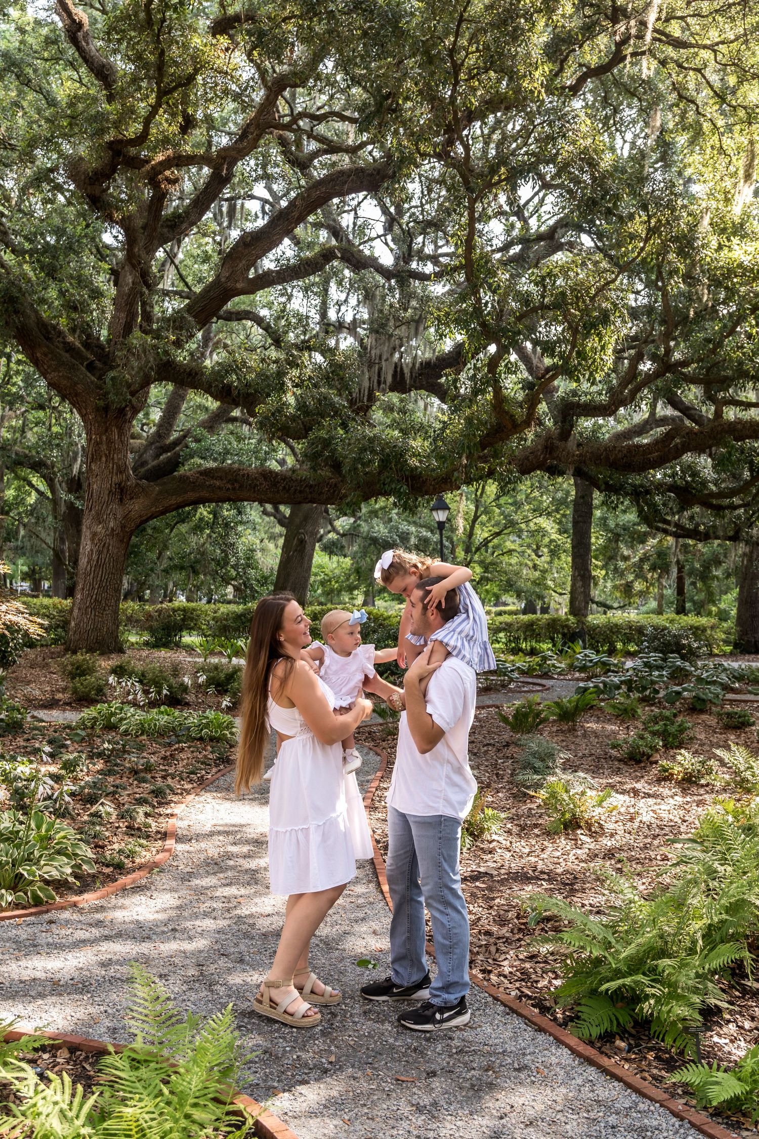 Family of four enjoying a sunny day in a lush green park under sprawling oak trees draped with Spanish moss.