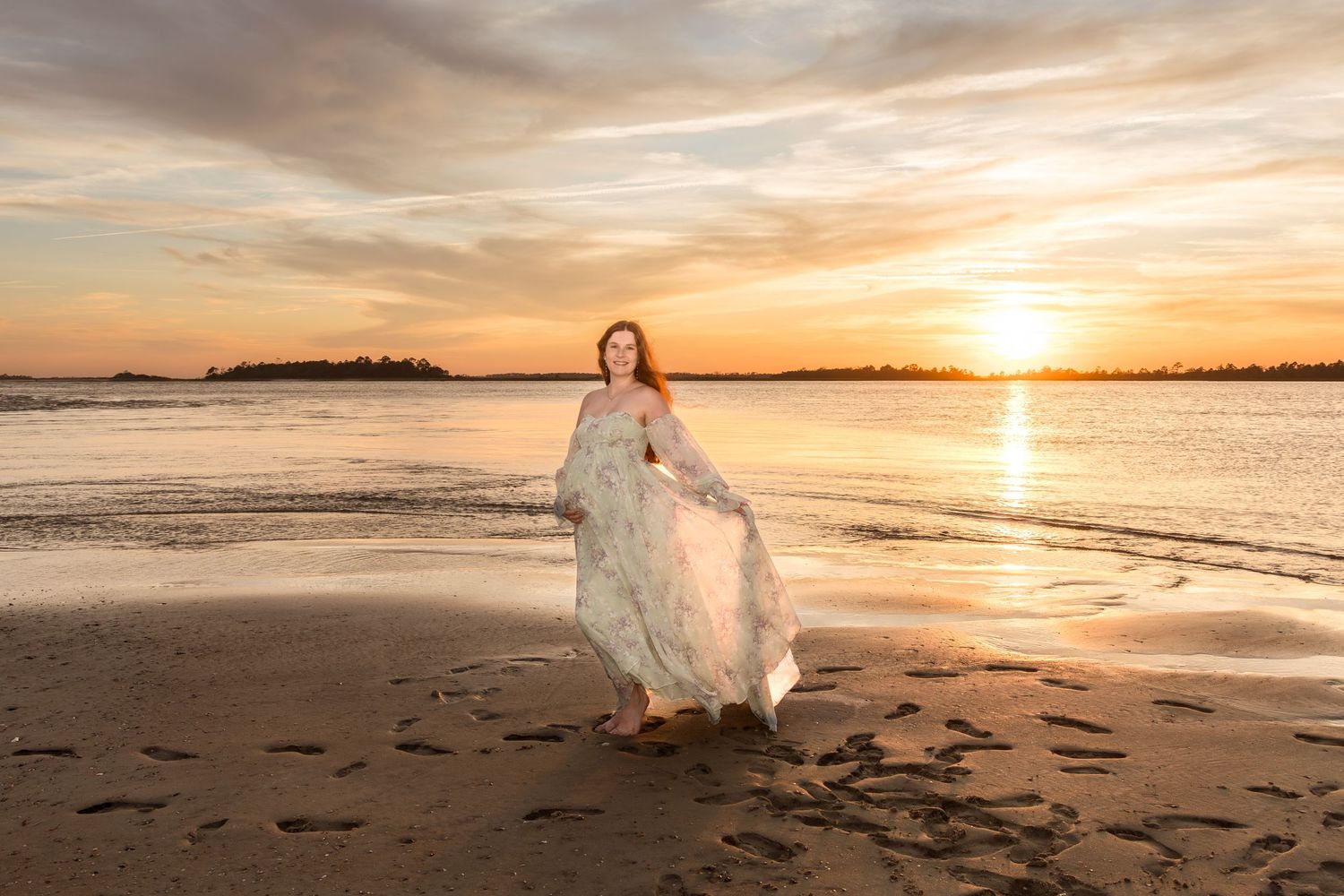 Woman in flowing gown walks on beach at golden sunset, waves reflecting warm orange sky behind her.