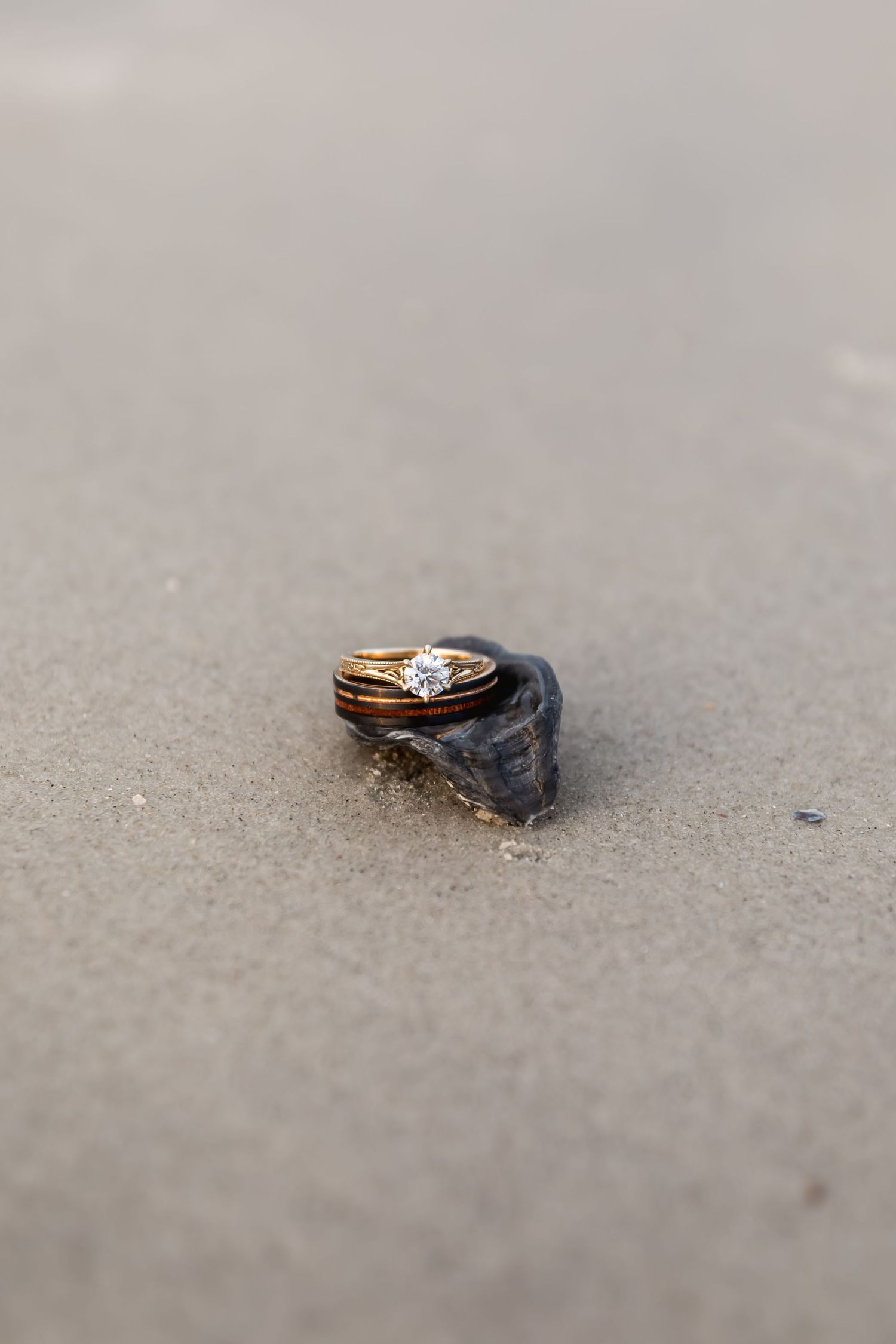 Gold diamond engagement and wedding rings resting on small rock in beach sand.