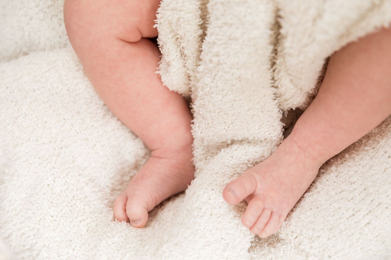 Small baby feet nestled in soft white plush blanket showing tiny toes against cozy fabric texture.