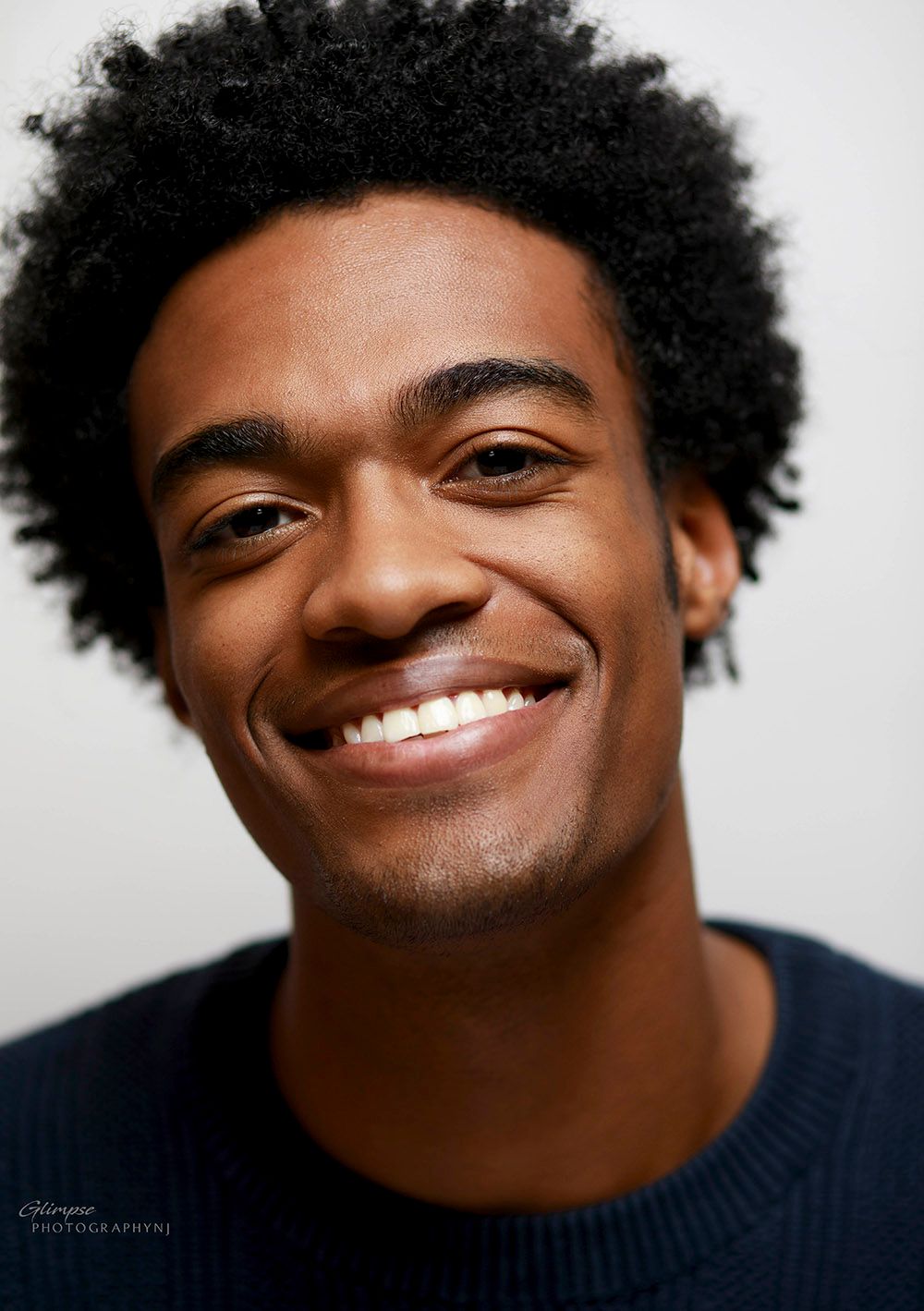 Smiling male actor with dark afro posing for professional headshot with white background