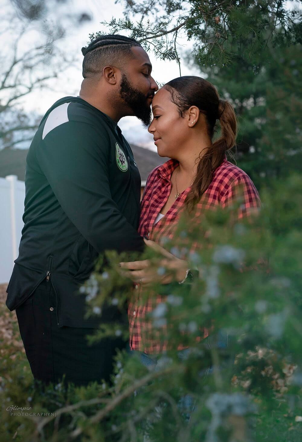 man wearing green shirt kissing woman on forehead underneath oak tree