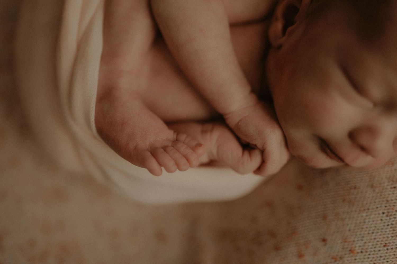 Artistic newborn portrait in gentle sepia tones on textured fabric.
