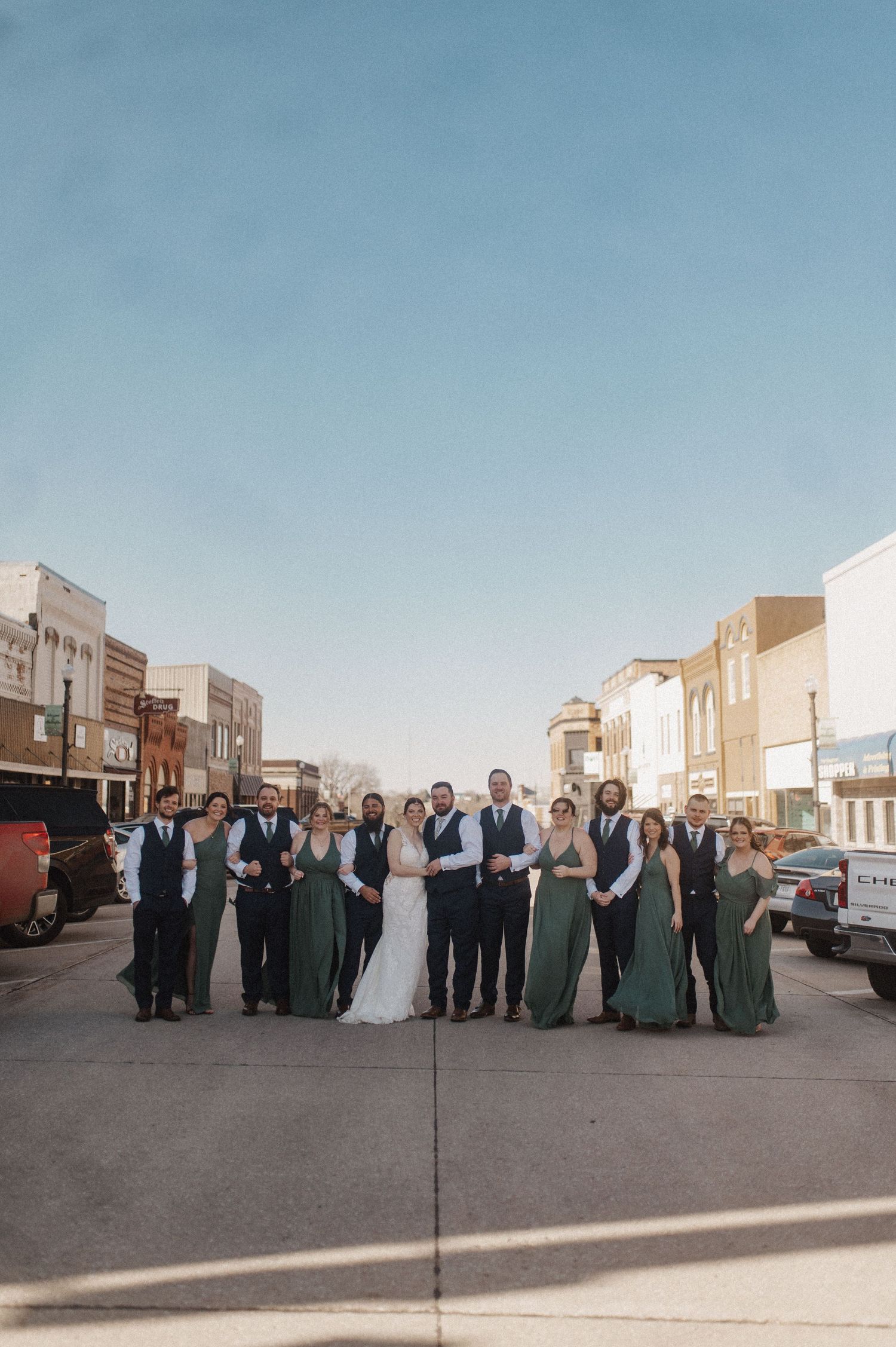 Wedding party poses together outside a vintage small town main street on a sunny day.