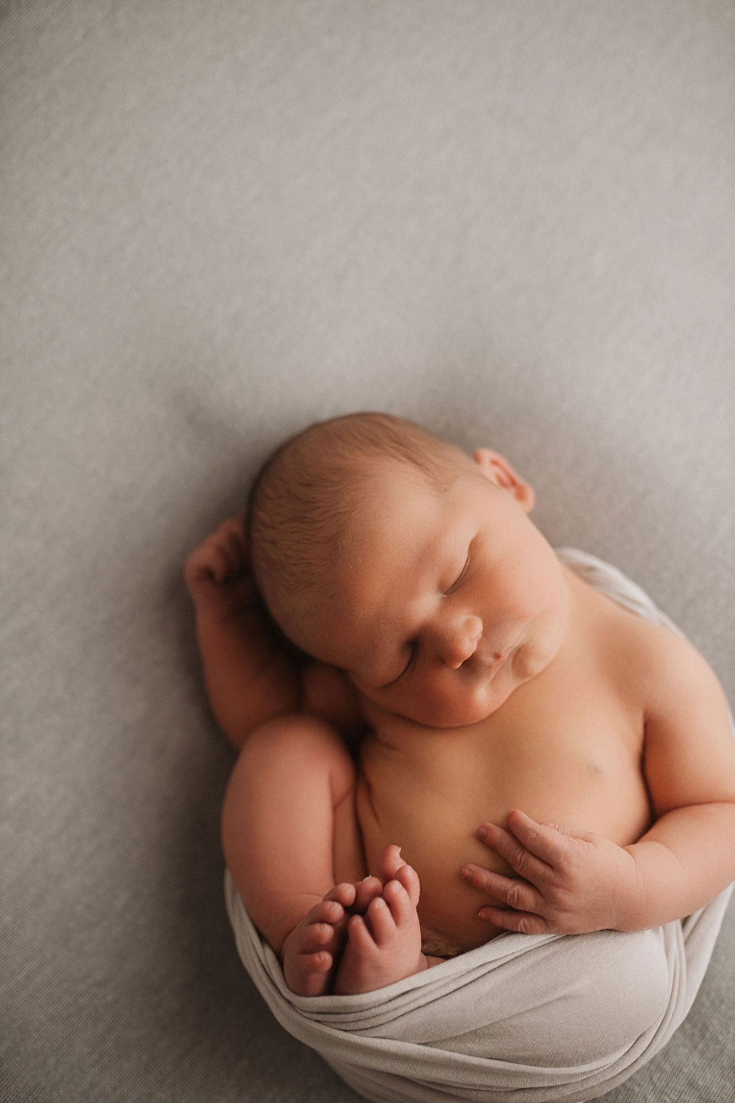 Peaceful sleeping newborn baby wrapped in soft gray fabric against neutral background.