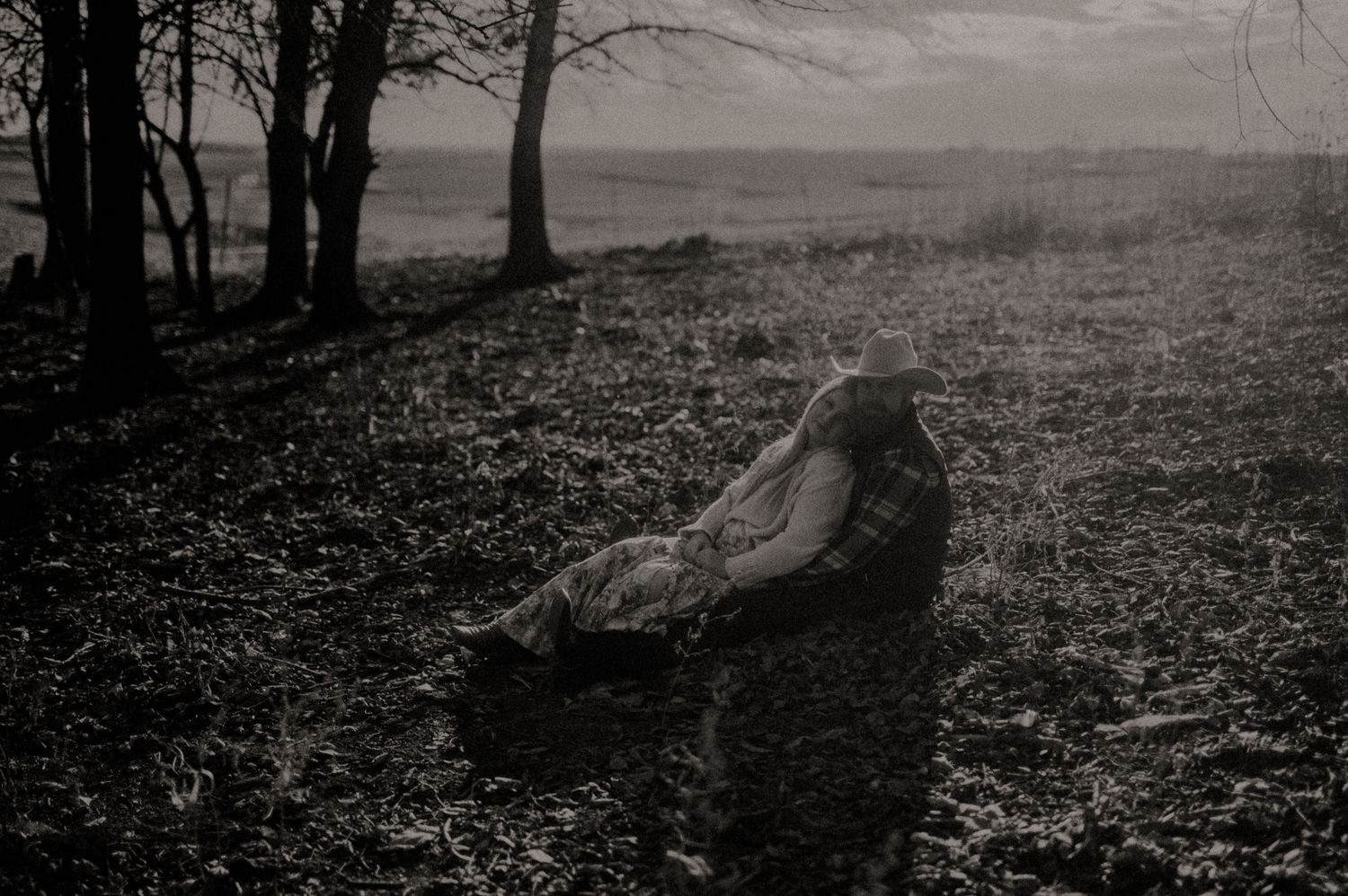 A misty landscape with silhouetted trees and rolling hills in black and white.