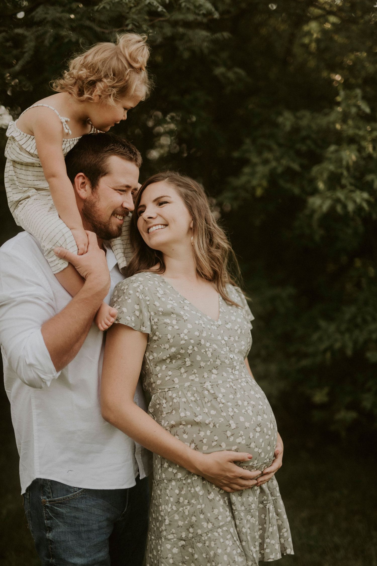 A couple shares an intimate moment outdoors in a series of romantic maternity photos with a natural backdrop.