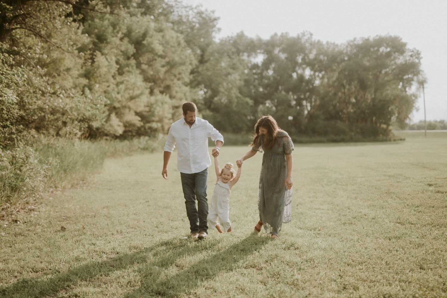 A family walks together through a sunlit meadow on a warm summer evening.