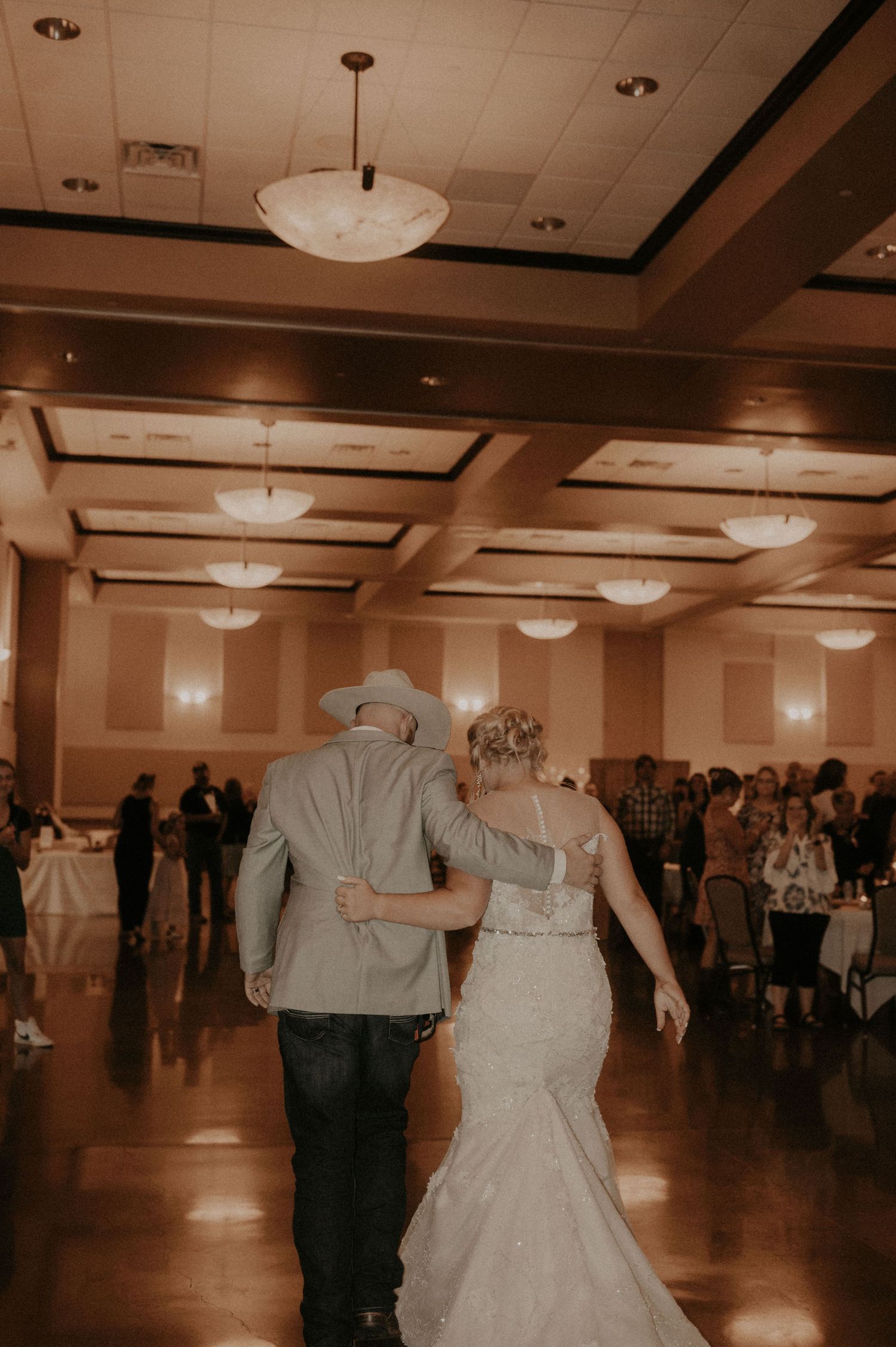 A romantic first dance sequence between newlyweds at a wedding reception with guests watching from the sides of the ballroom.