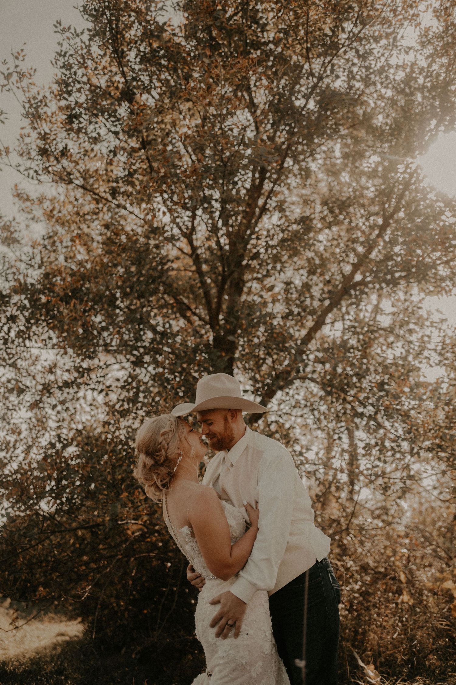 A romantic couple shares an intimate moment in a sunlit forest setting during golden hour.