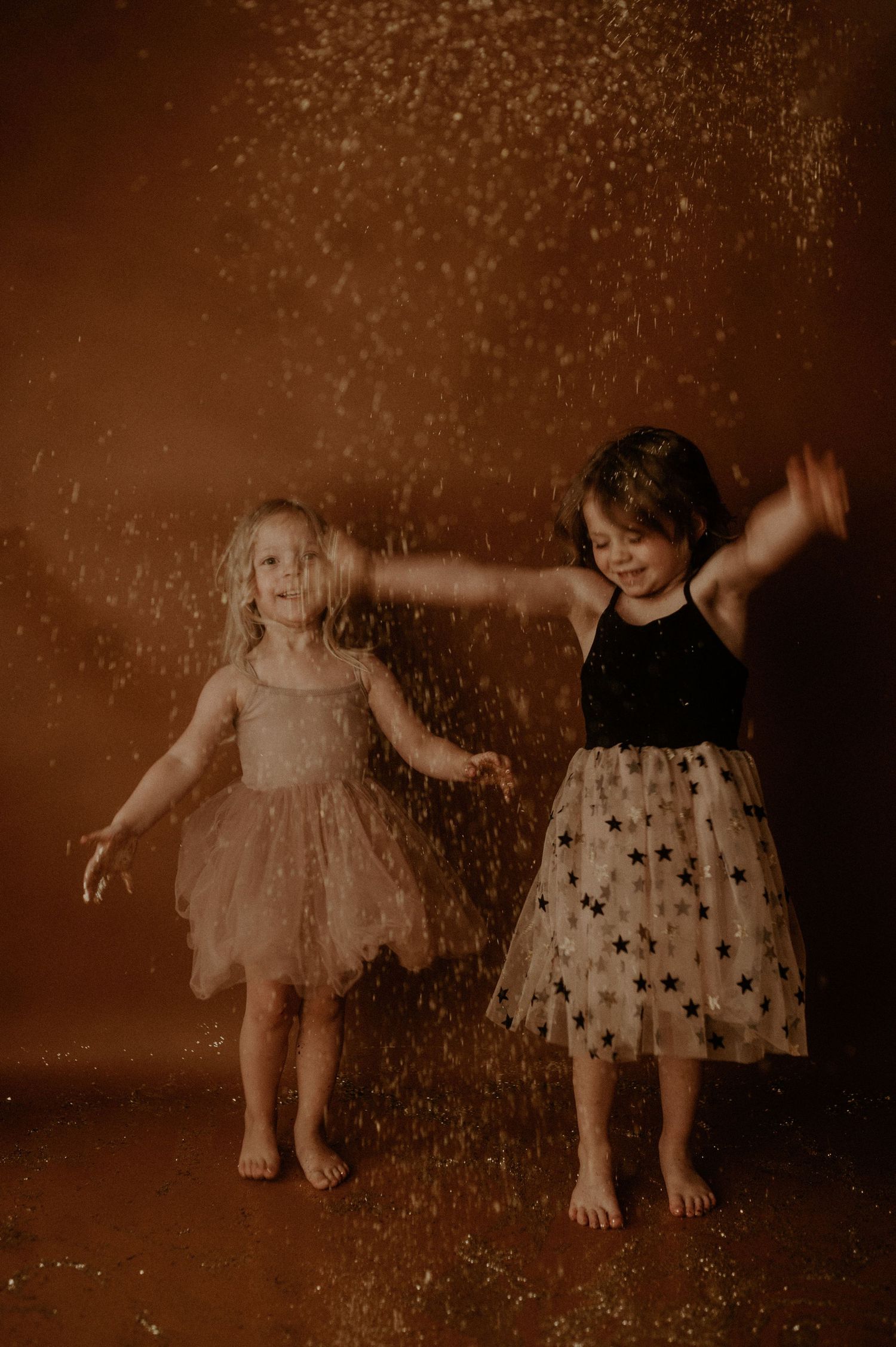 Two young children in vintage-style dresses play together in a sepia-toned portrait series.