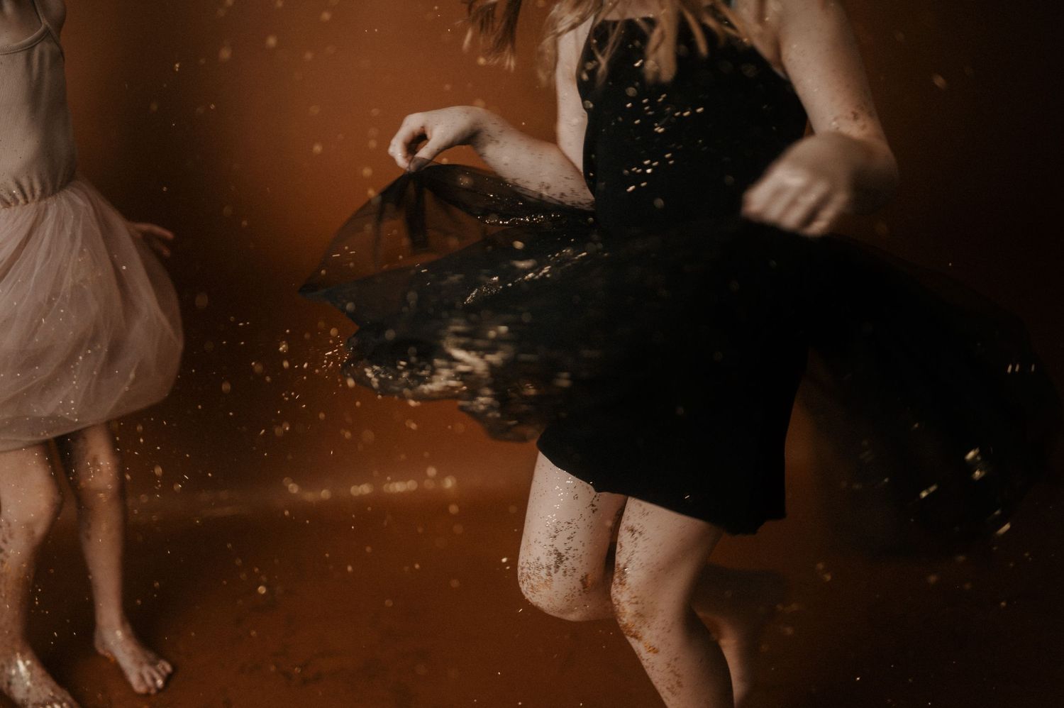 Two people in dresses dance and twirl together in a dark room with glittering particles in the air.