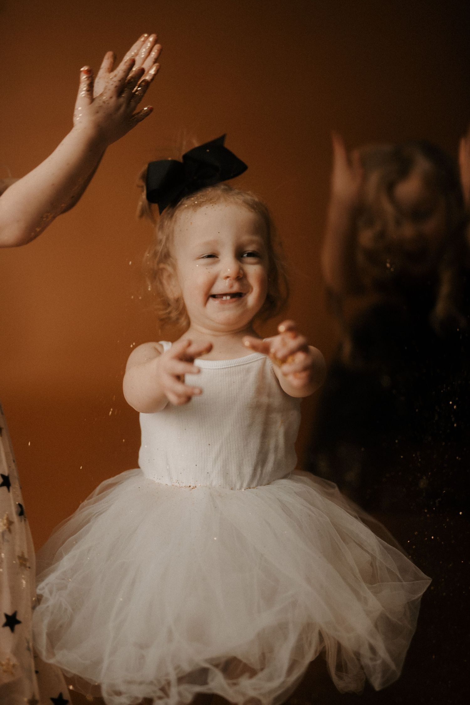 A series of photos showing a small child in a white tulle dress dancing and twirling against a warm brown background.