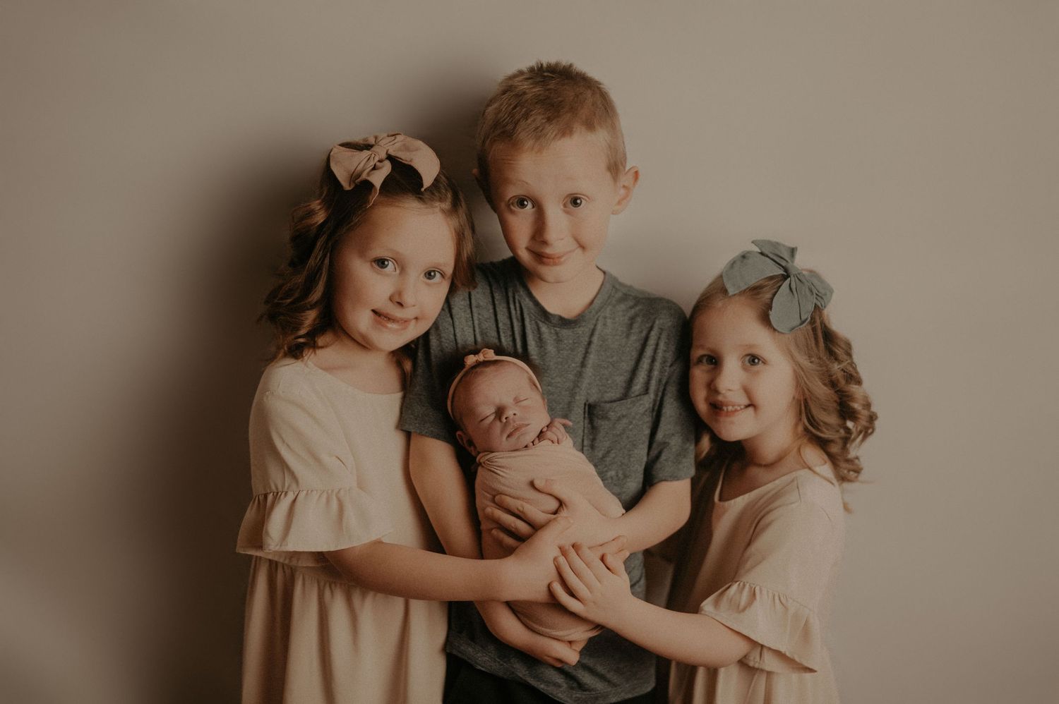 Children embracing and smiling together in soft neutral colored clothing.