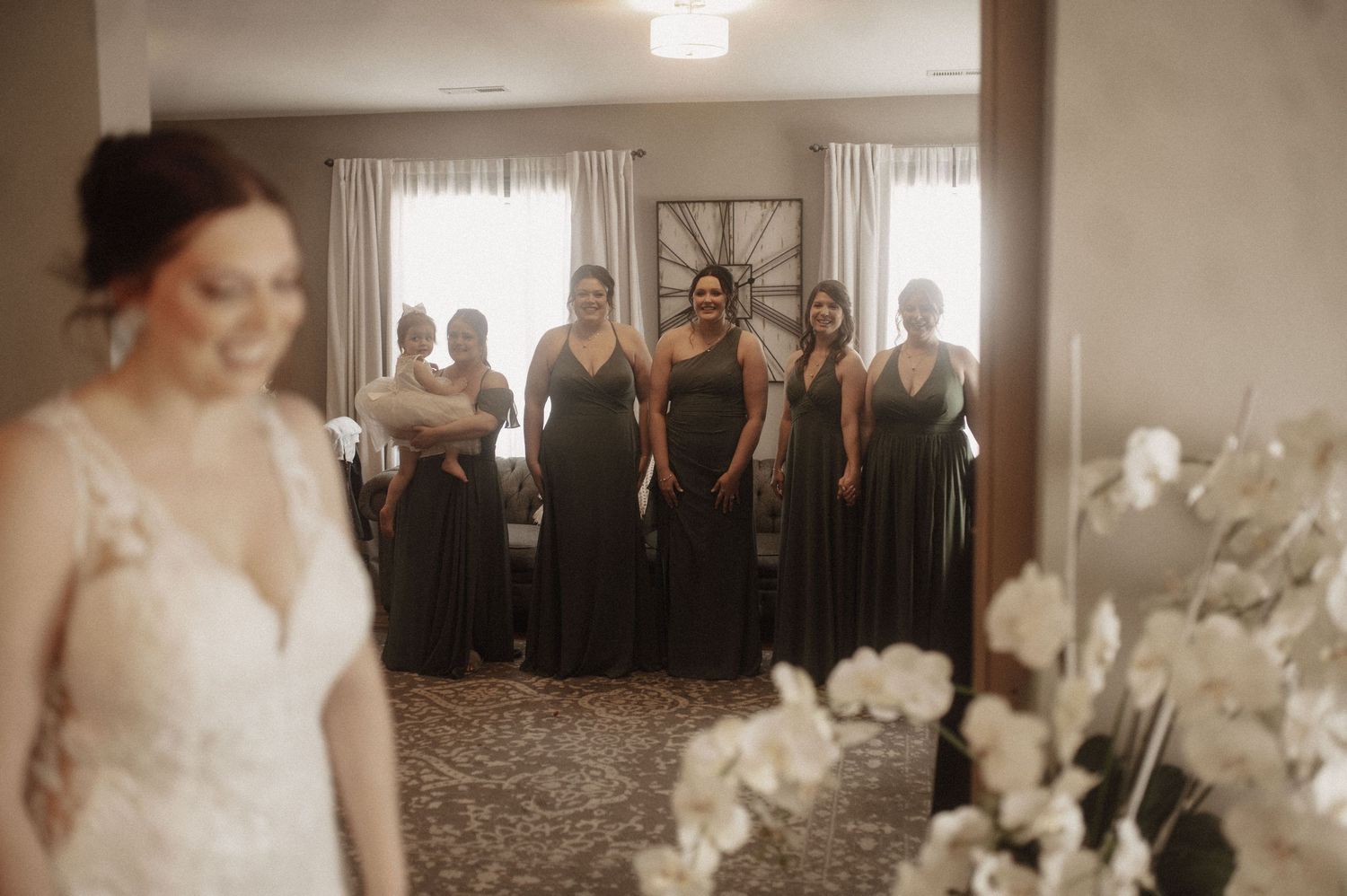 A group stands together in a well-lit room with white curtains and hardwood flooring.