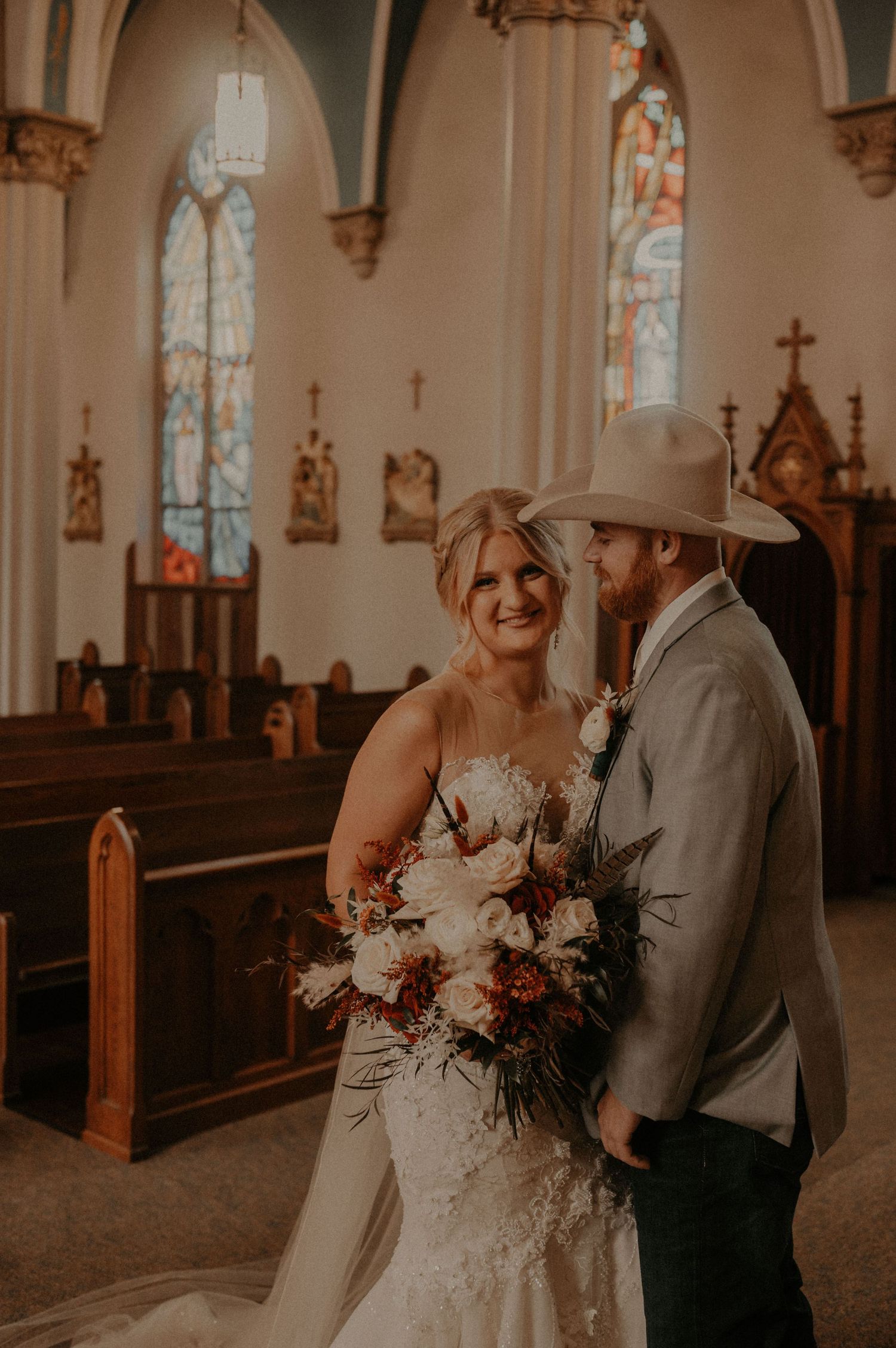 Cowboy hat wearing couple shares joyful moment during church wedding photos.