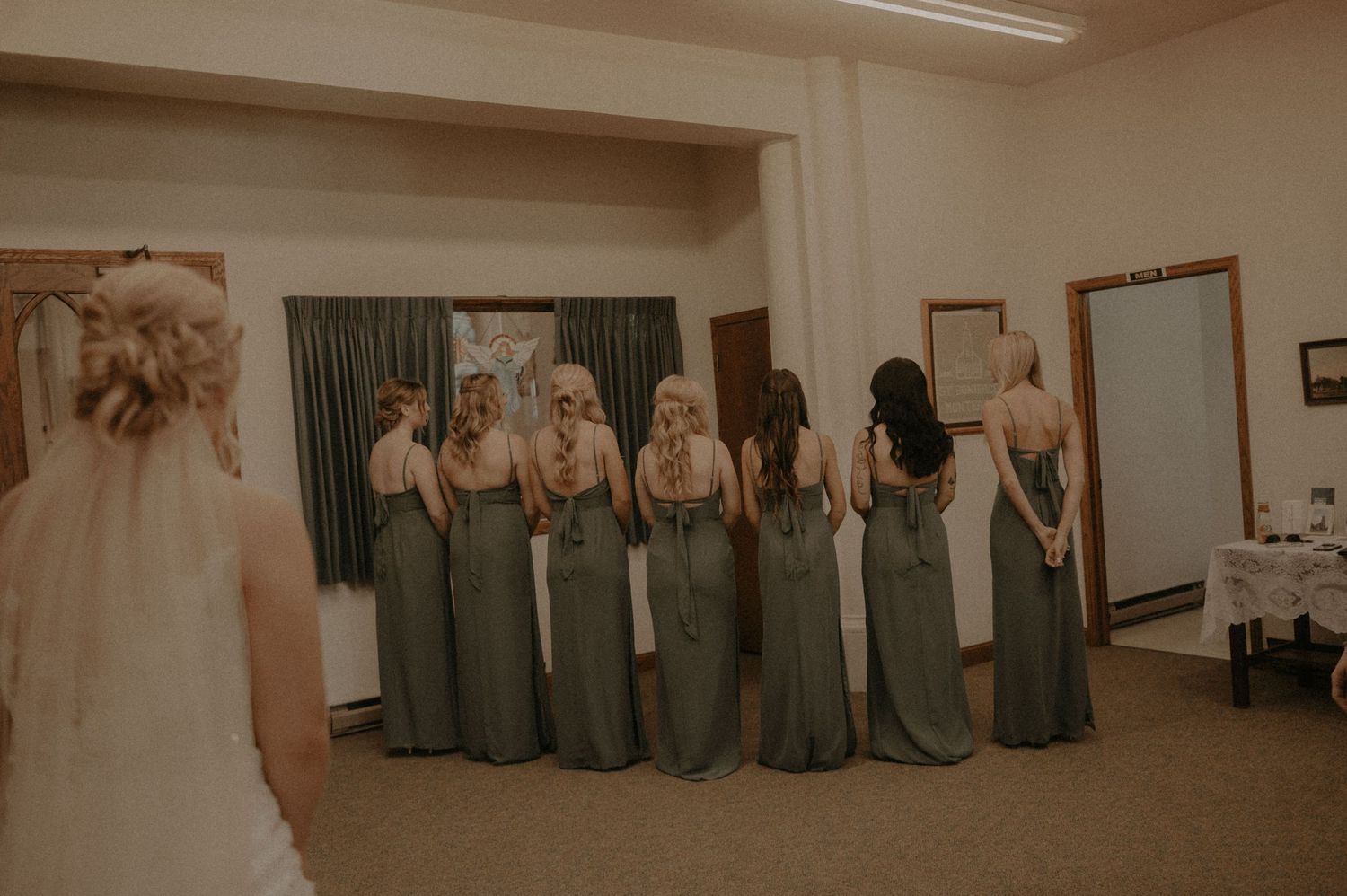 Wedding party members in gray dresses lined up against a wall.