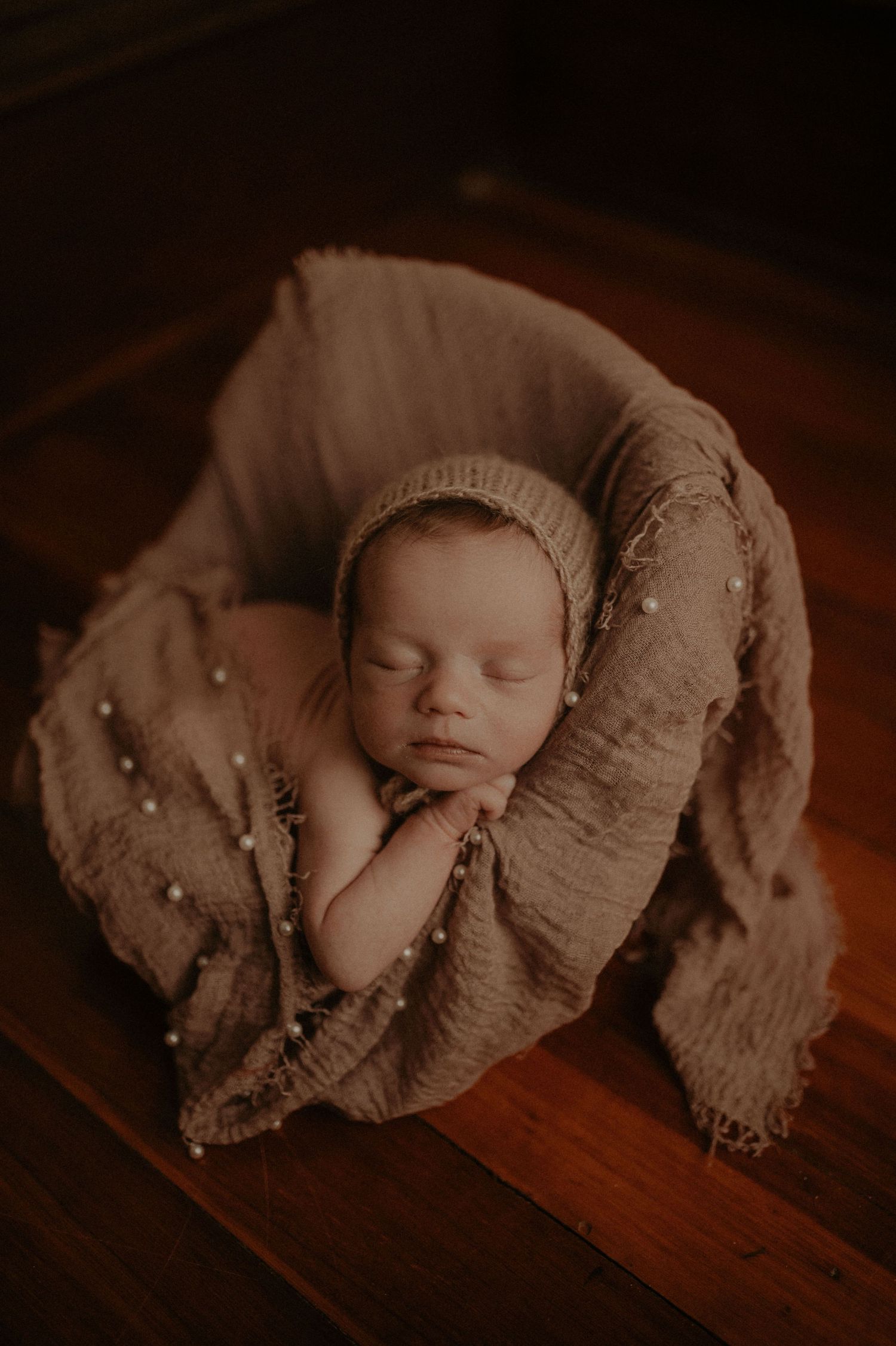 Vintage-style newborn portrait on wooden surface with textured wrap.