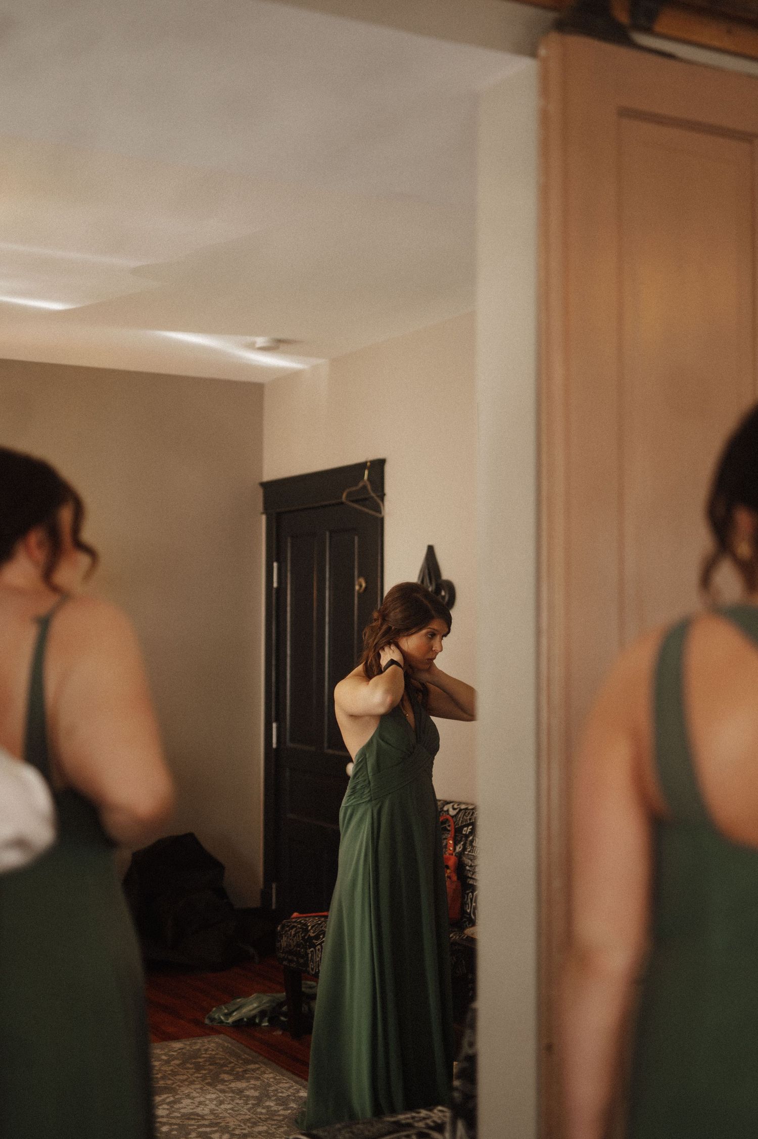 Bridesmaids in emerald green dresses preparing in a brightly lit room.