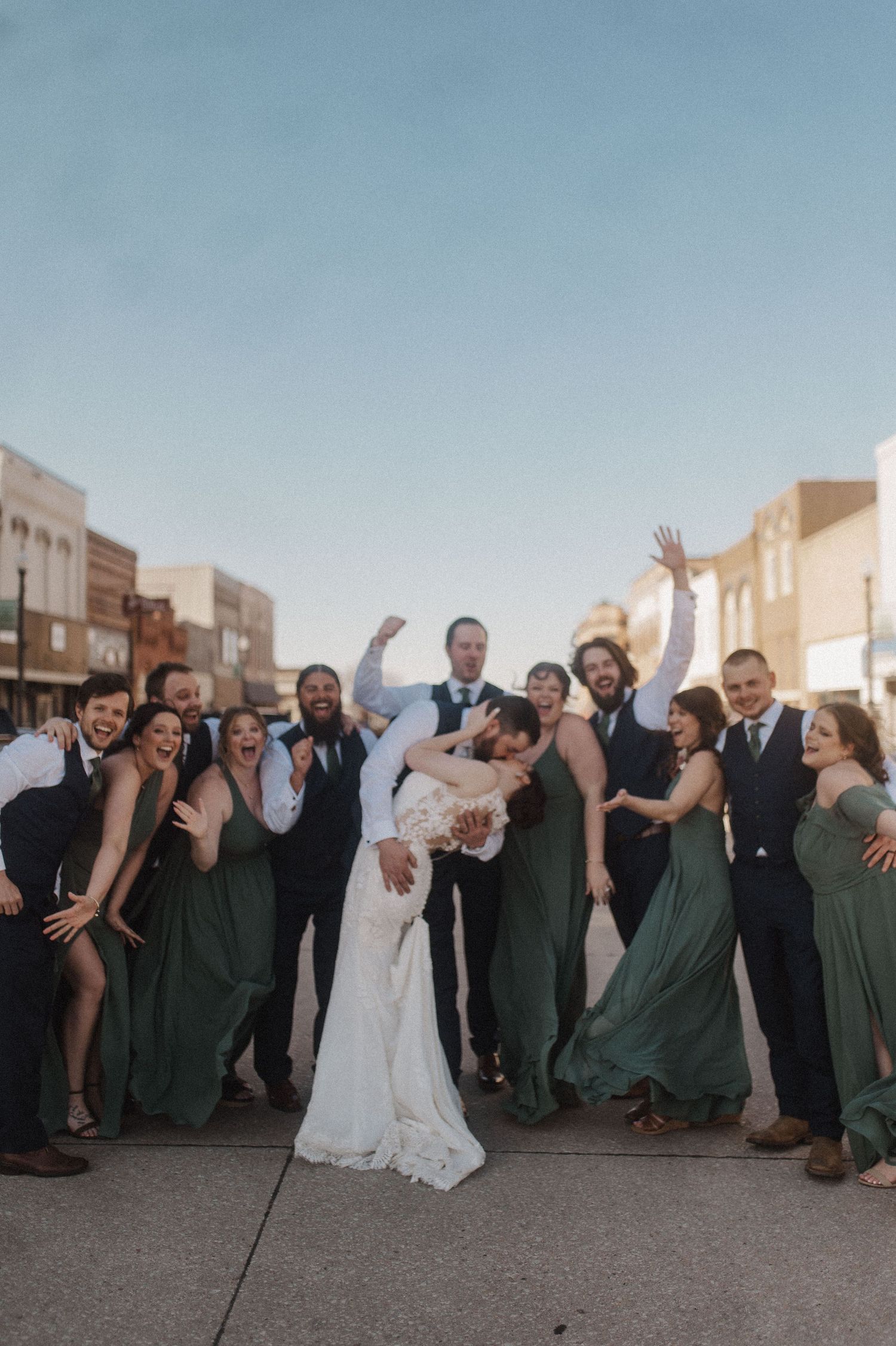 Wedding party strikes fun poses outside historic brick buildings during sunset.