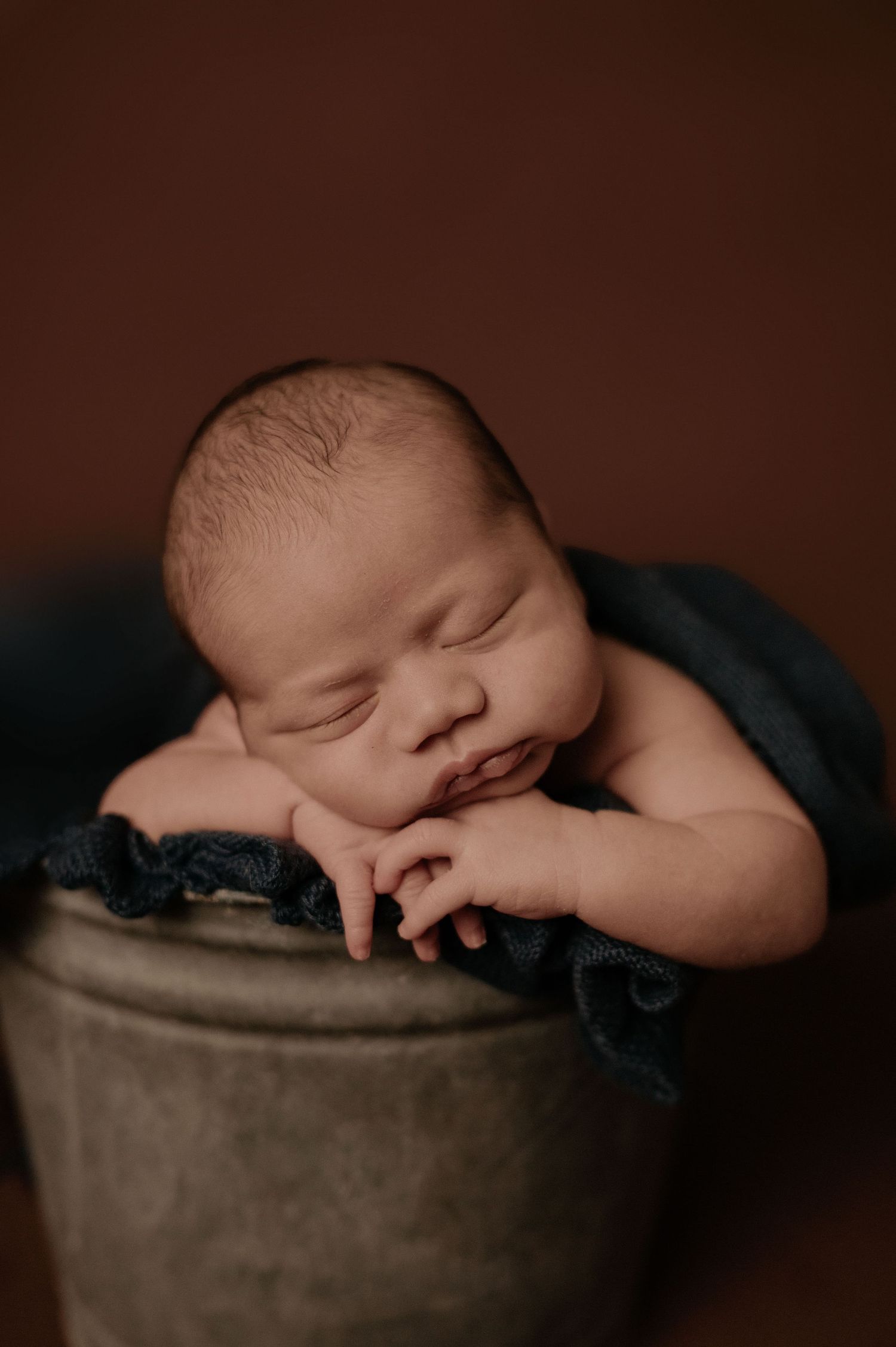 Peaceful newborn sleeping on round cushion in moody studio lighting.