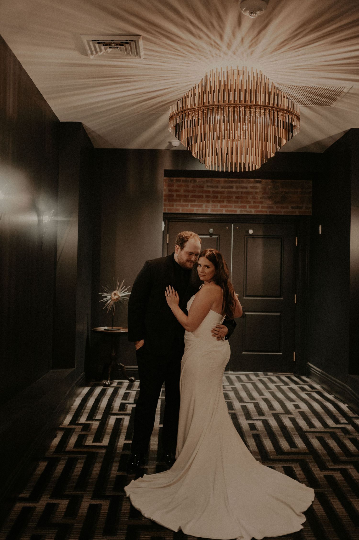 A couple dances together on a black and white geometric patterned floor beneath ornate chandeliers.