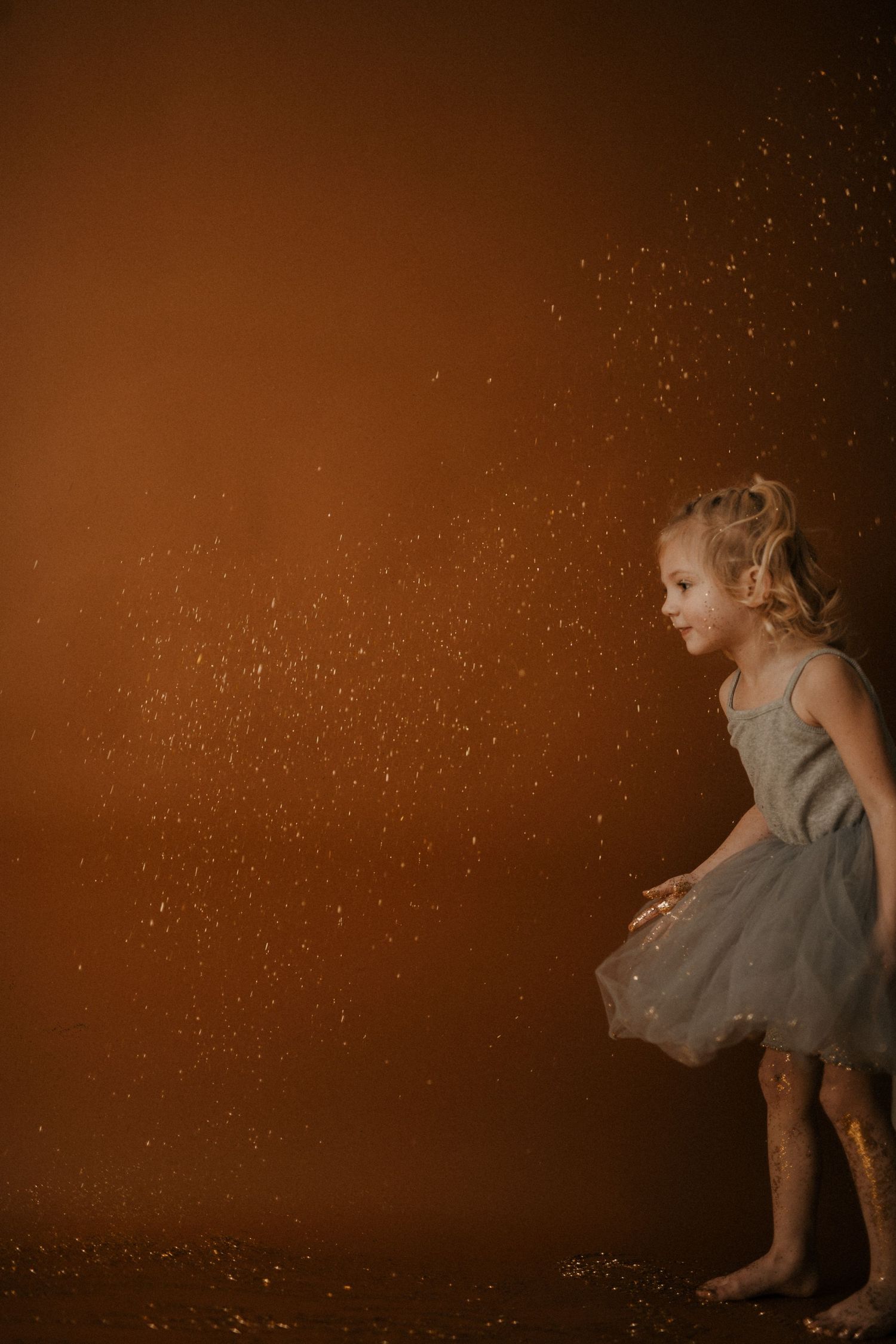 A small child in a gray dress twirls and dances against a warm brown background with sparkling lights.