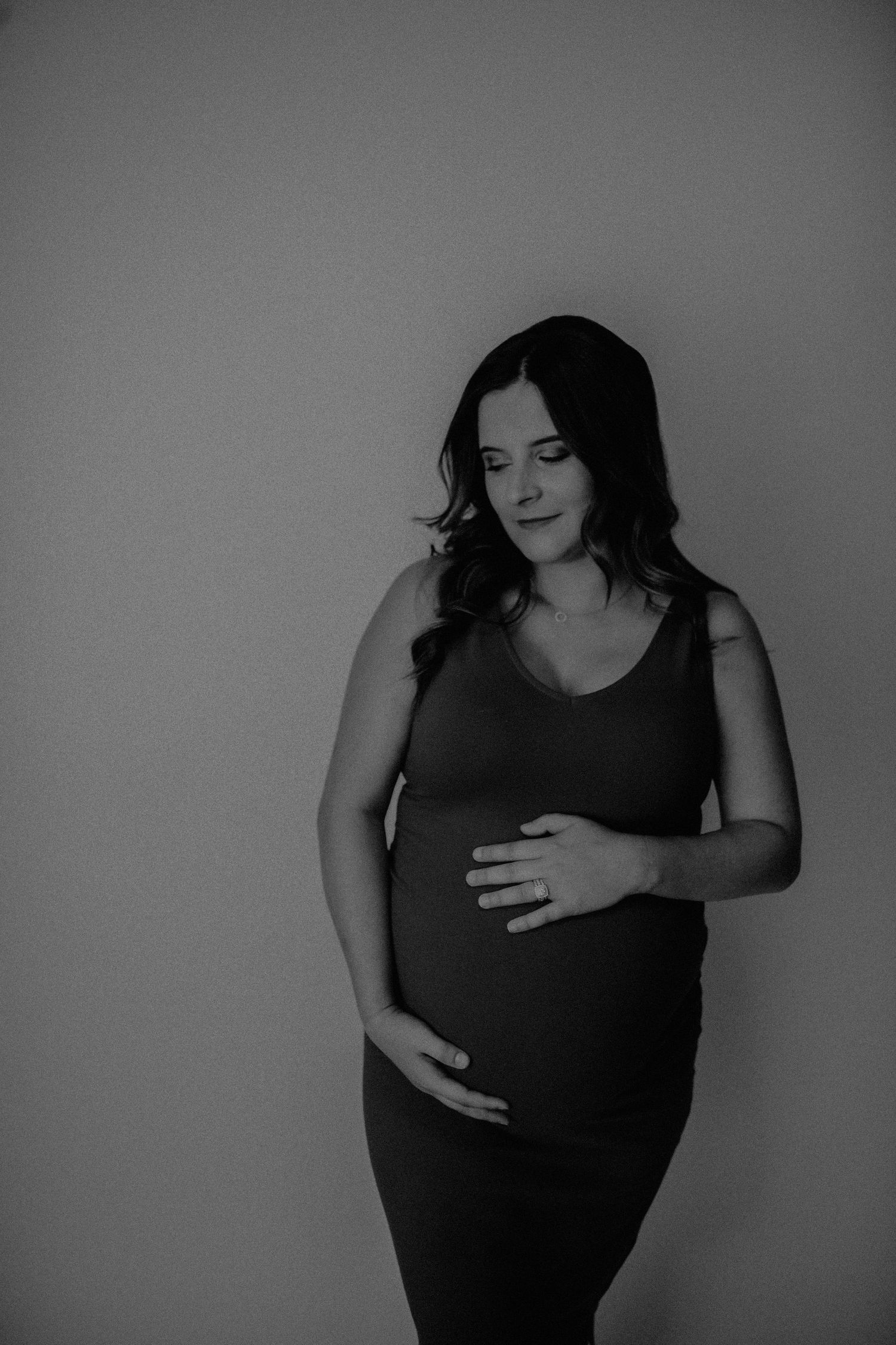 Black and white maternity photo series showing progression of pregnancy with woman in dark dress against plain background.