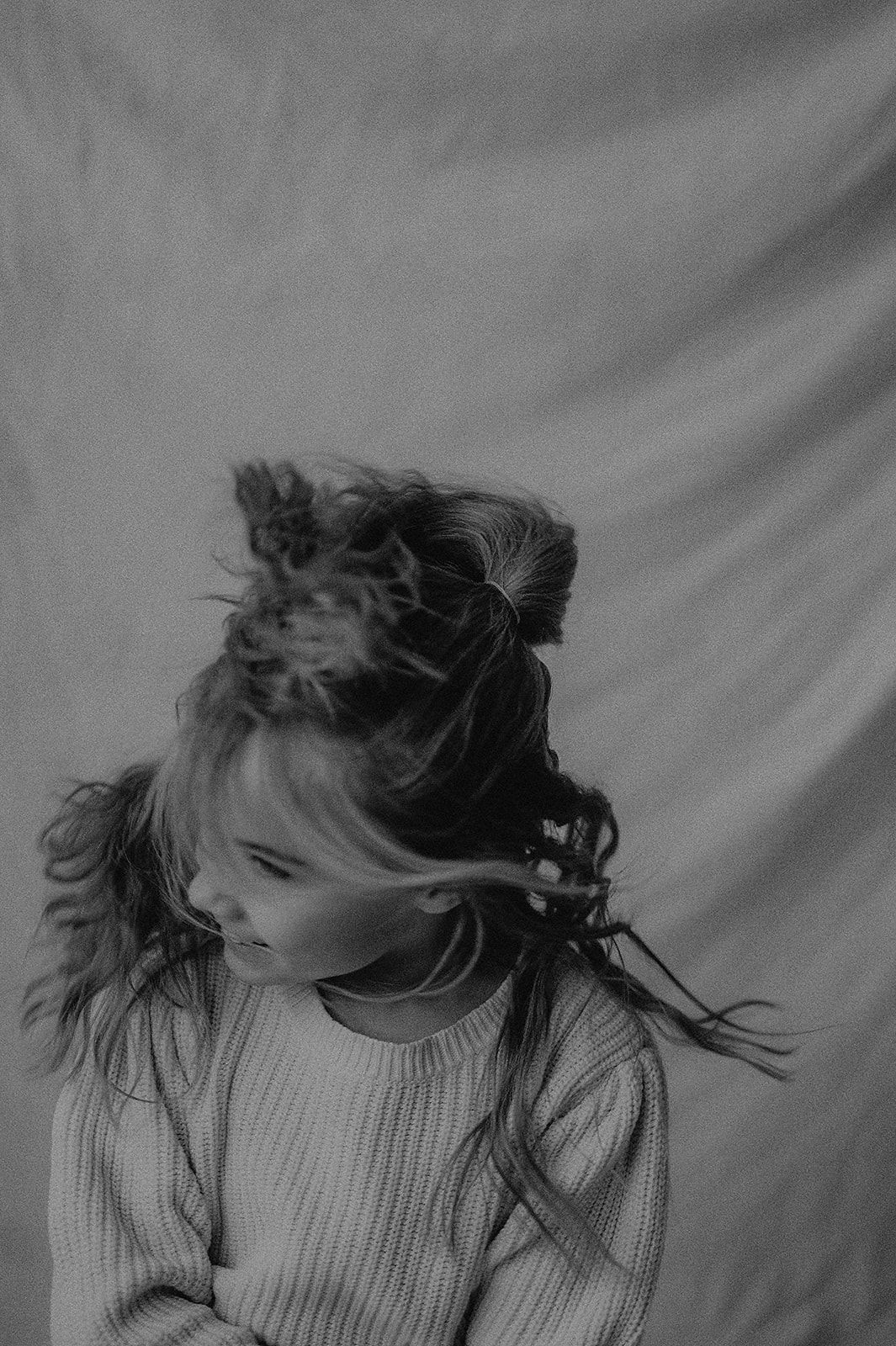 Black and white portrait of windswept hair against light background with subject wearing ribbed sweater.
