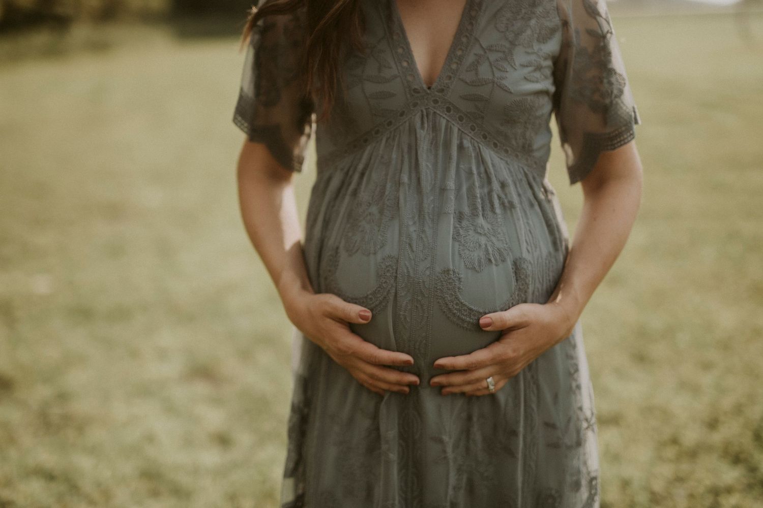 A maternity photo series showing a pregnant woman in a grey dress posing in a sunlit field.