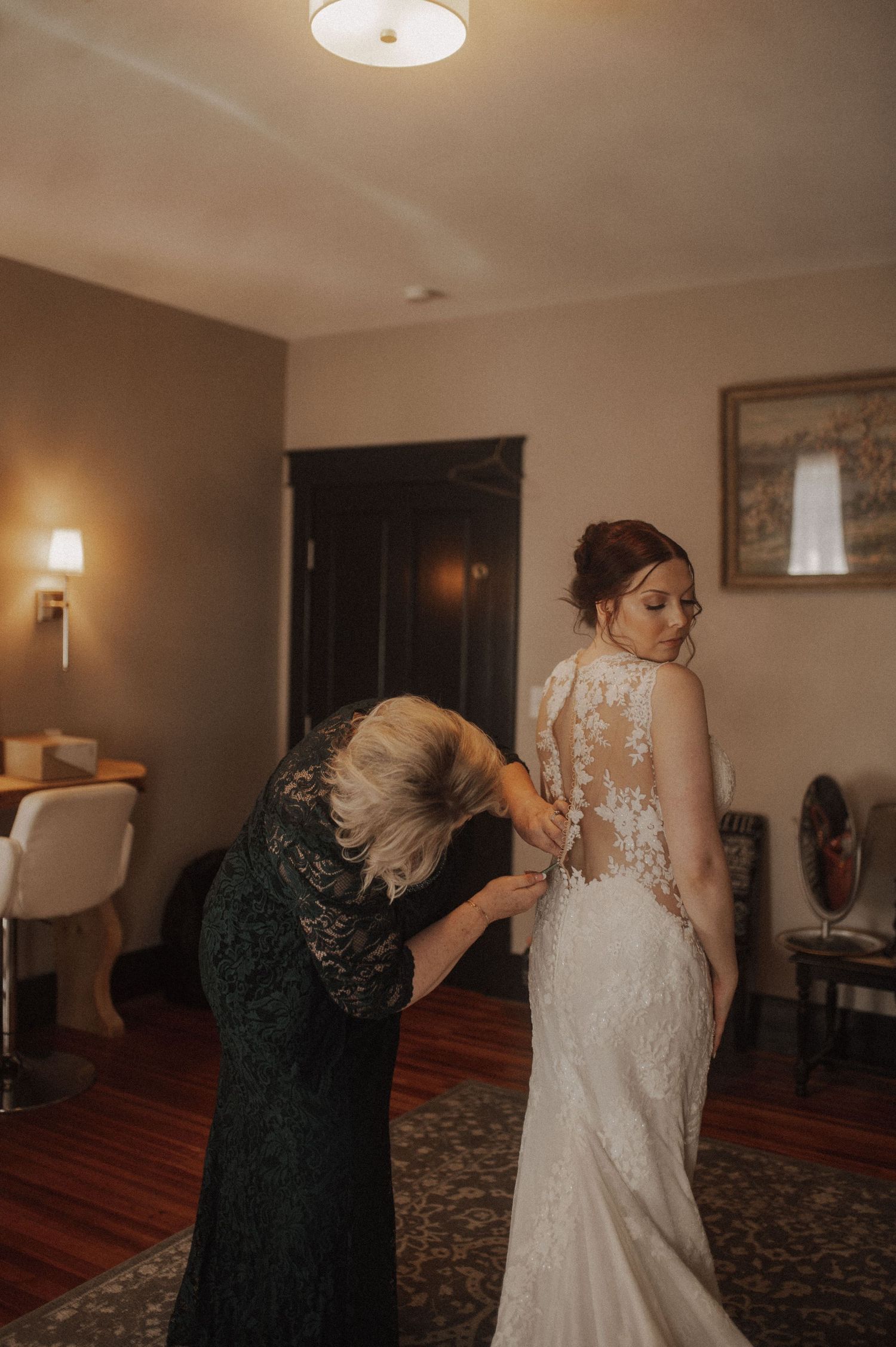 A series of photos showing someone helping a bride get dressed in an elegant lace wedding gown in a warmly lit room.