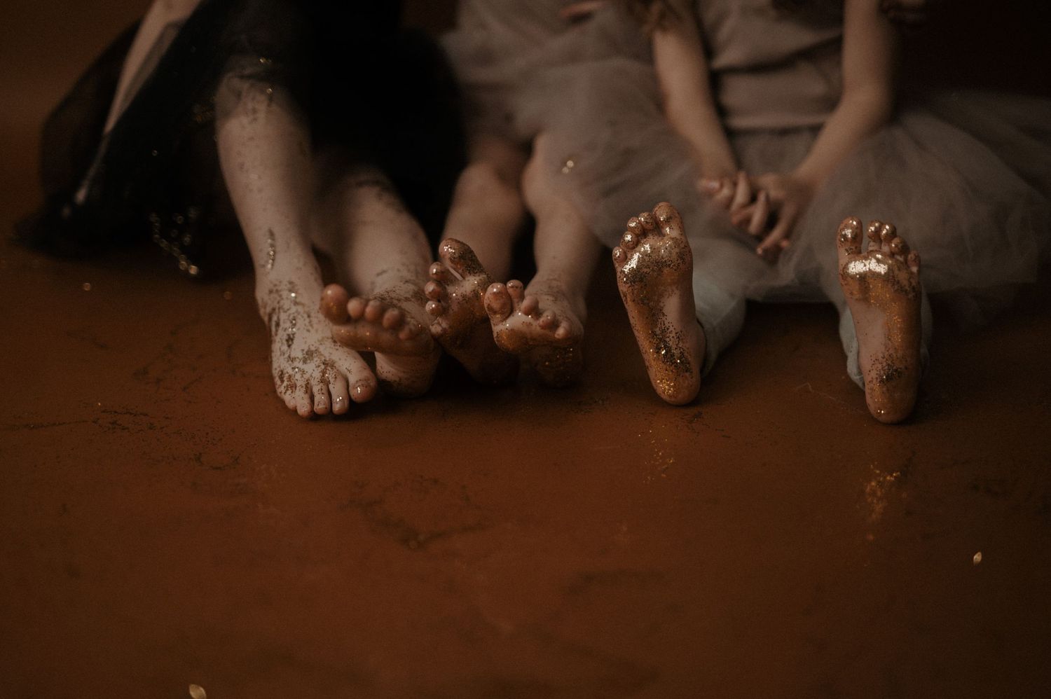 A row of bare feet lined up along a dark wooden floor in warm lighting.