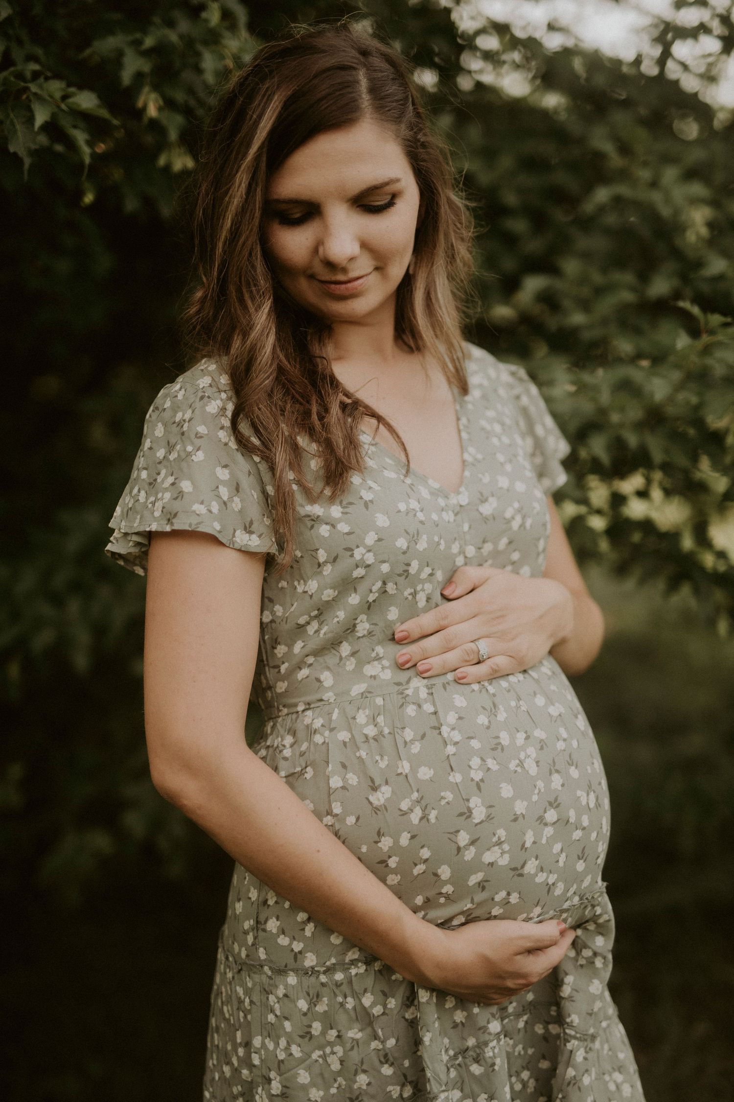 Expectant mother in a floral dress poses in a garden setting during golden hour maternity photoshoot.