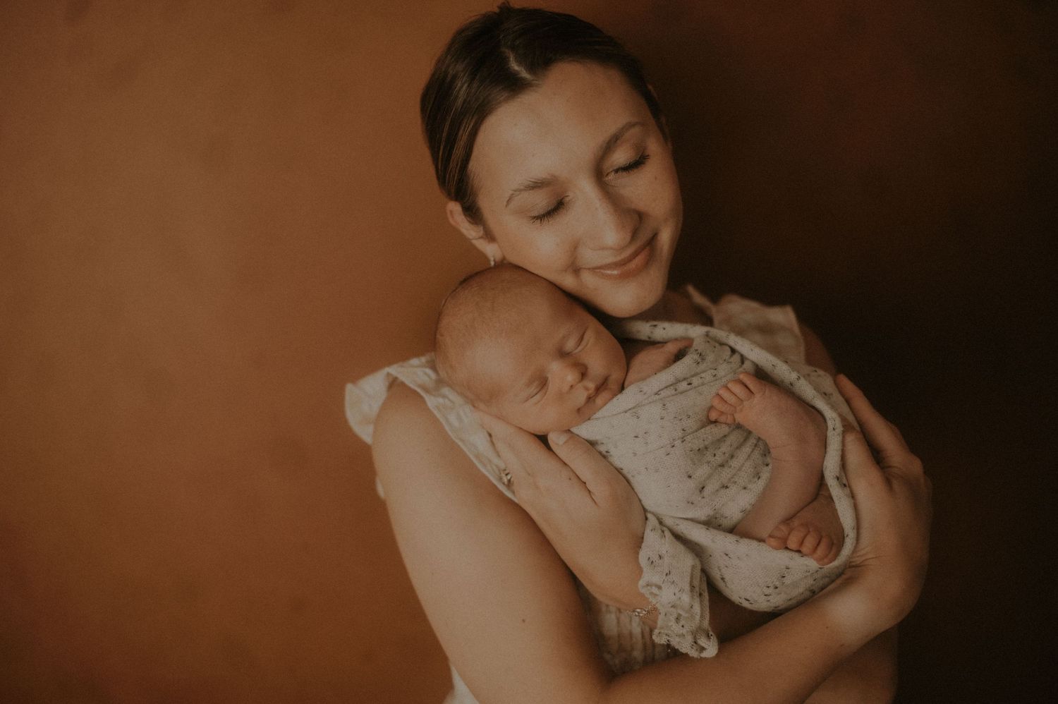A tender moment between parent and infant in warm sepia tones.