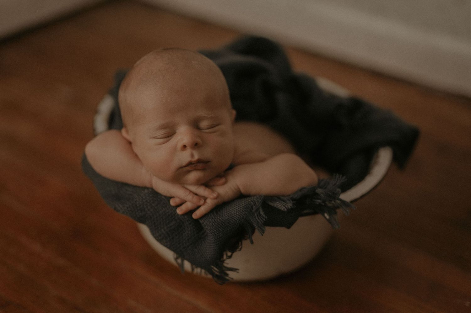 A sleeping baby rests peacefully on a dark wooden floor with soft lighting and warm tones.