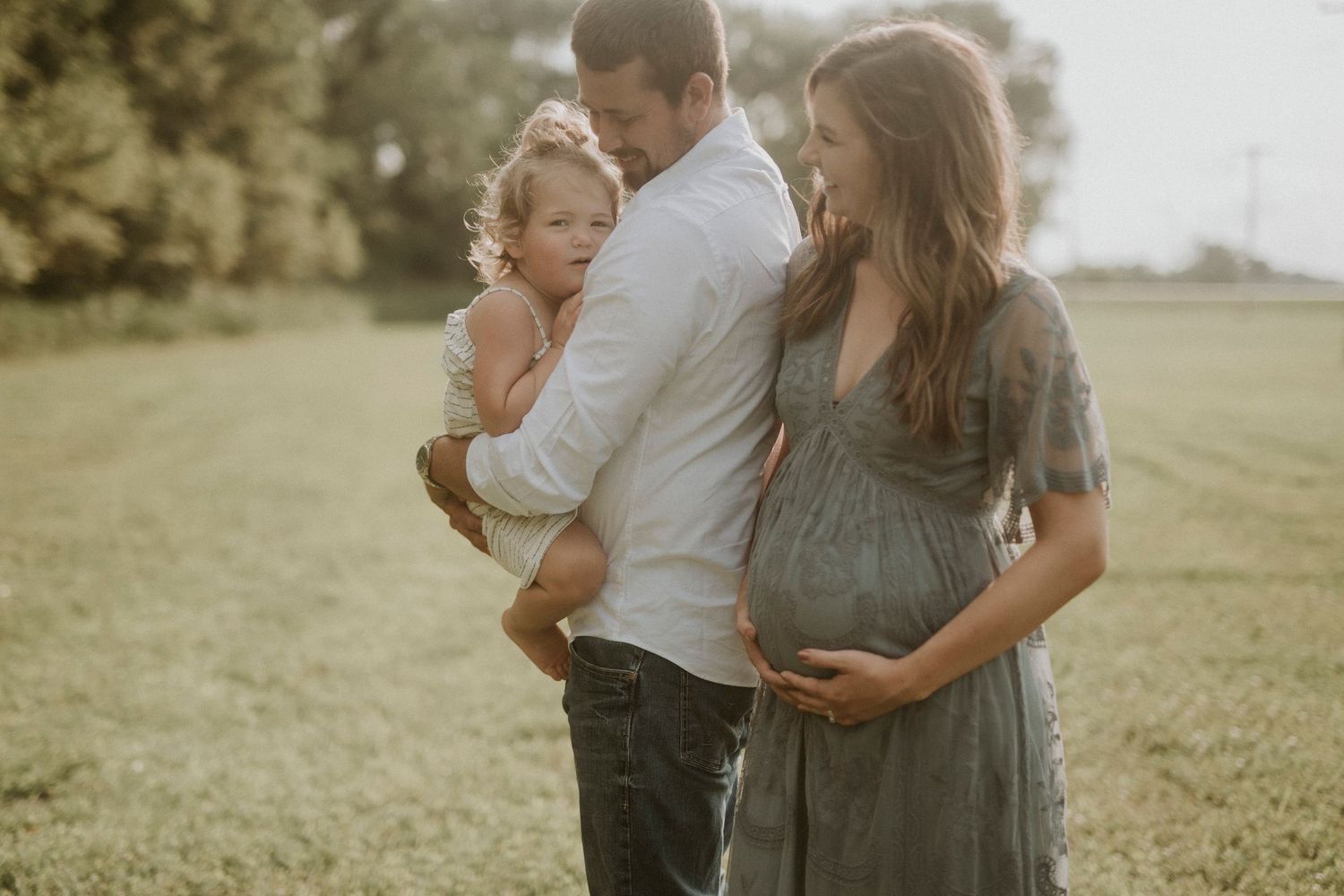 A family shares tender moments together in a sunny field during a warm summer evening photoshoot.