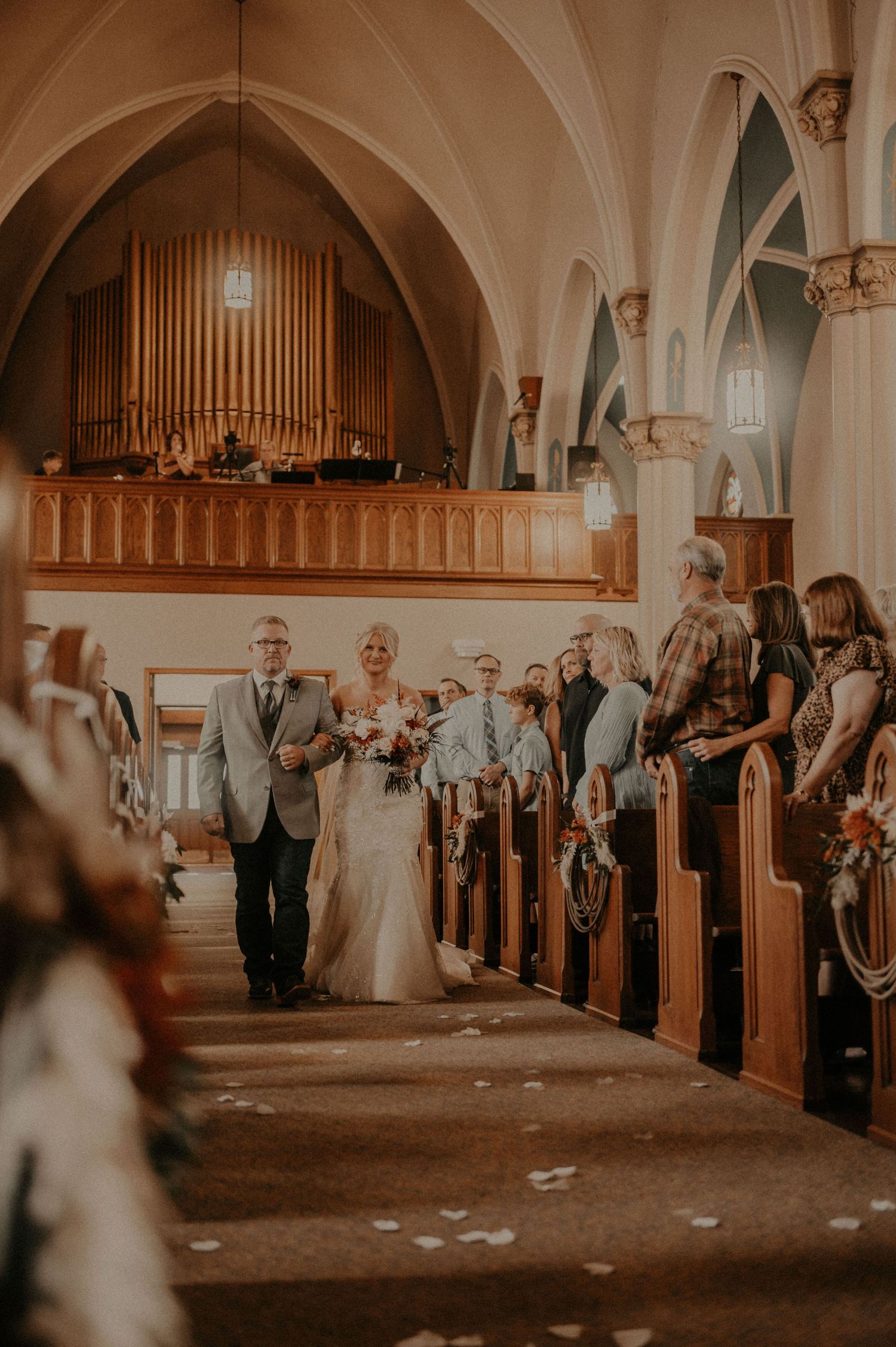 A traditional church wedding ceremony with guests seated in wooden pews beneath ornate vaulted ceilings and pipe organ.