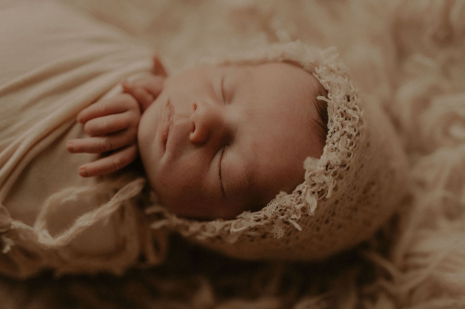Close-up profile of sleeping baby in vintage lace bonnet on plush surface.