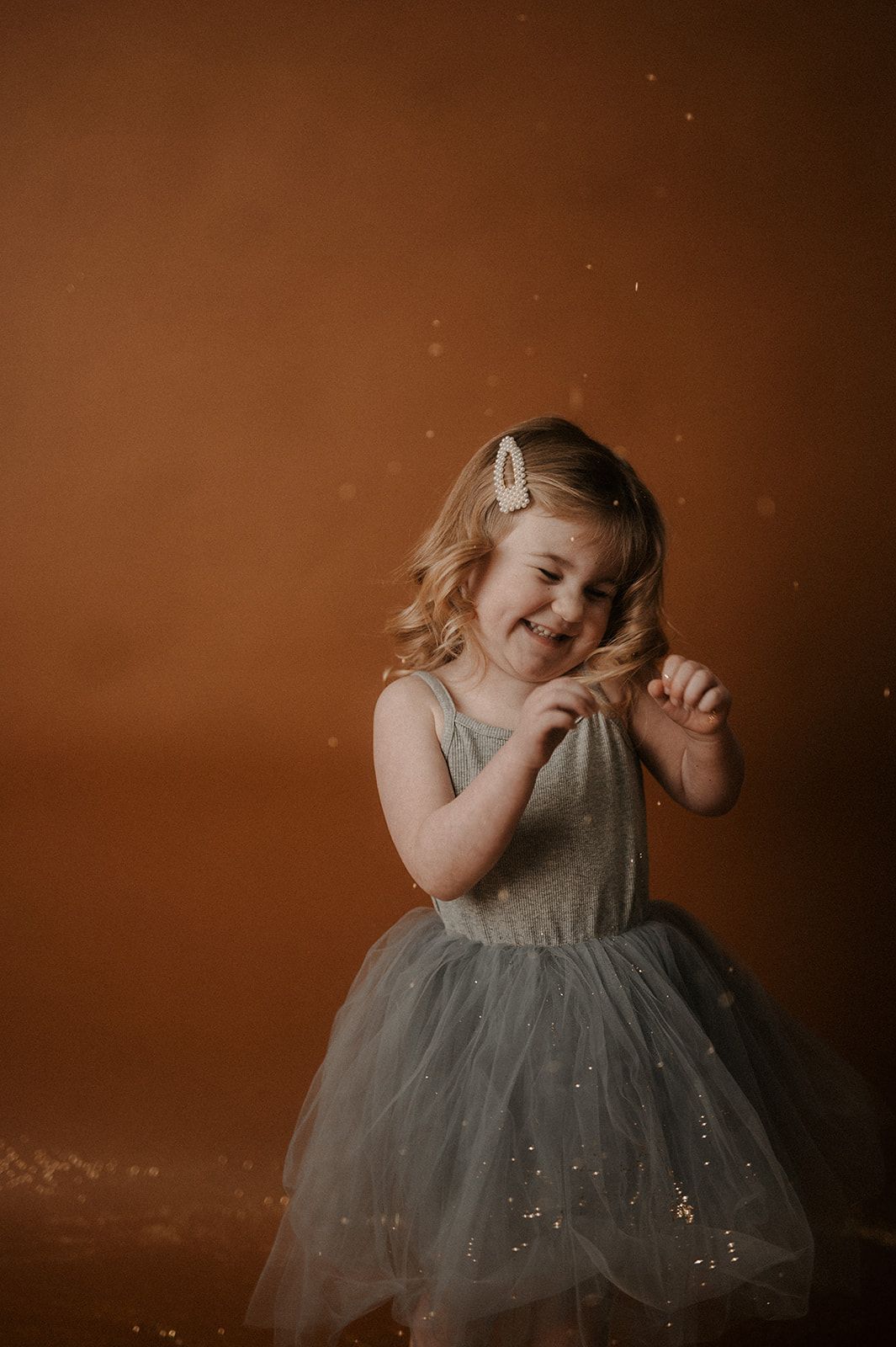A series of four photos showing a small child in a sparkly gray tulle dress playing and twirling against a brown backdrop.