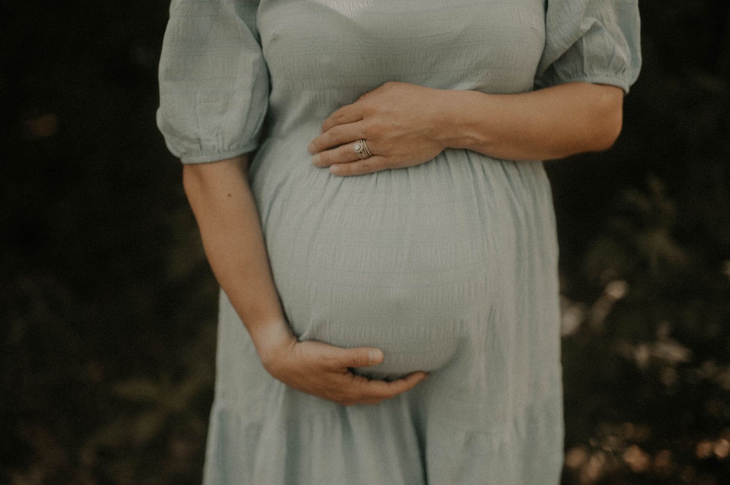 A maternity photo series showing a pregnant woman in a white dress cradling her belly against a dark background.