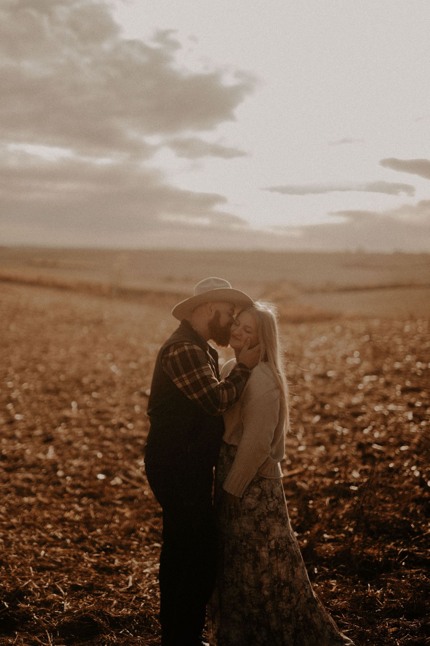 Silhouetted couple embraces in a romantic moment against a dramatic sunset over a rural field.