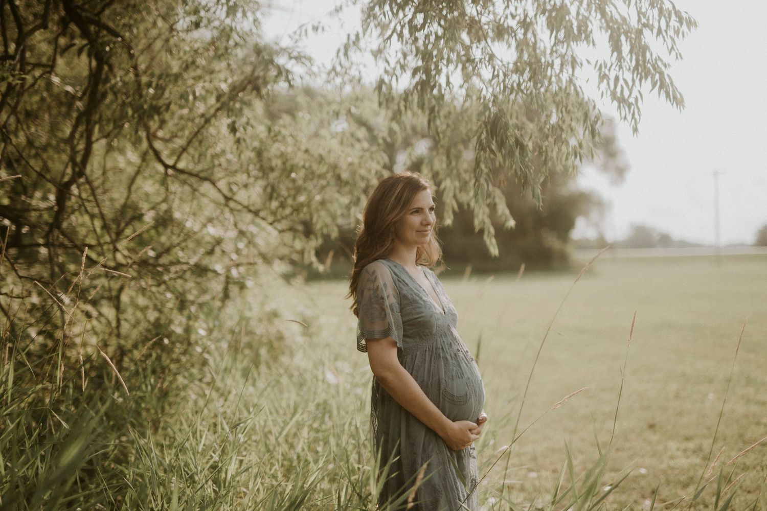 A couple embraces in a sunlit meadow with tall grass and trees creating a romantic, ethereal atmosphere.